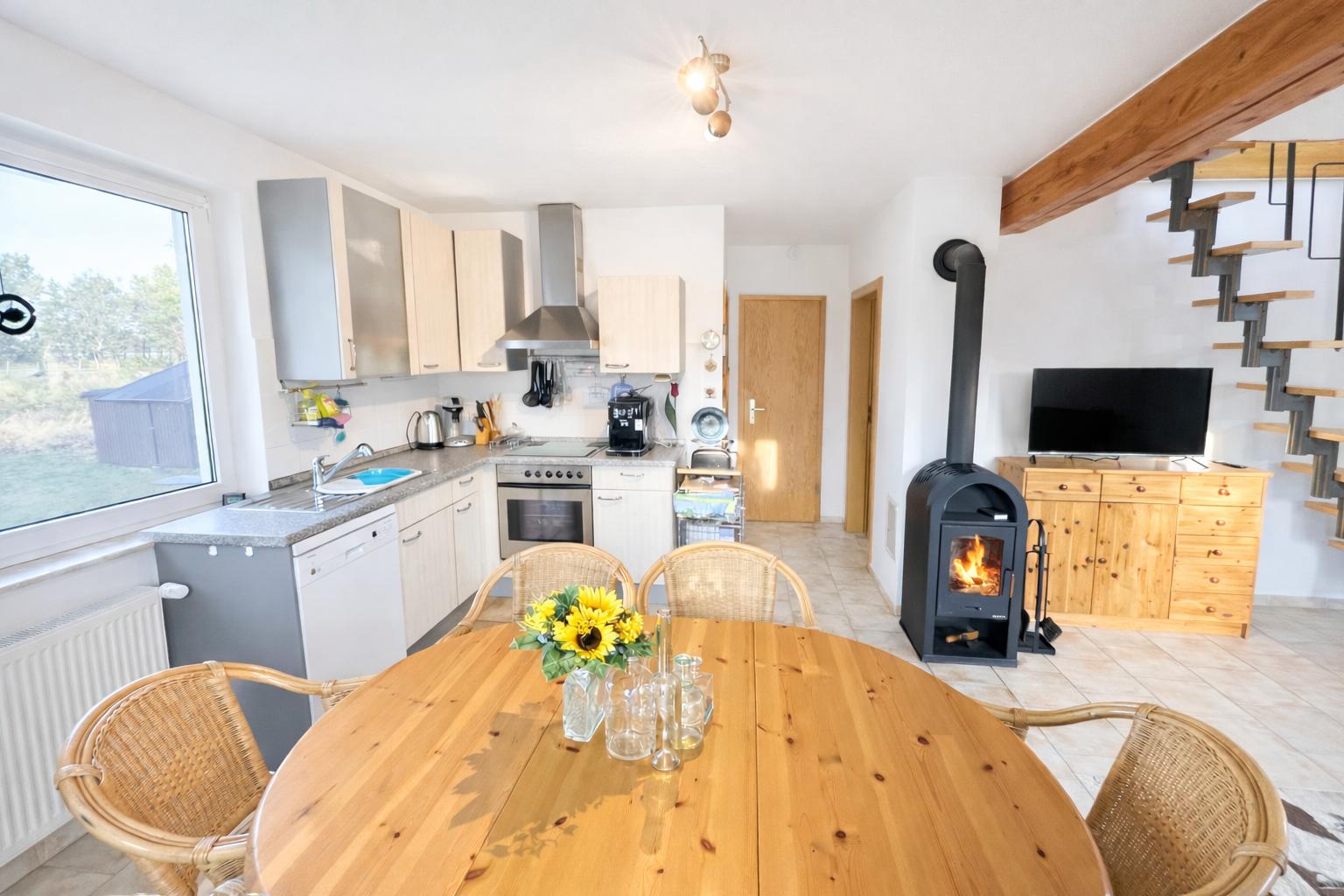 Küche mit Esstisch, Kaminofen und TV. Holzstufen führen zur oberen Etage.