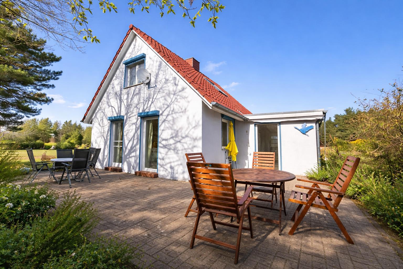Wohnhaus mit Terrasse, Garten und Holzmöbel unter blauem Himmel.