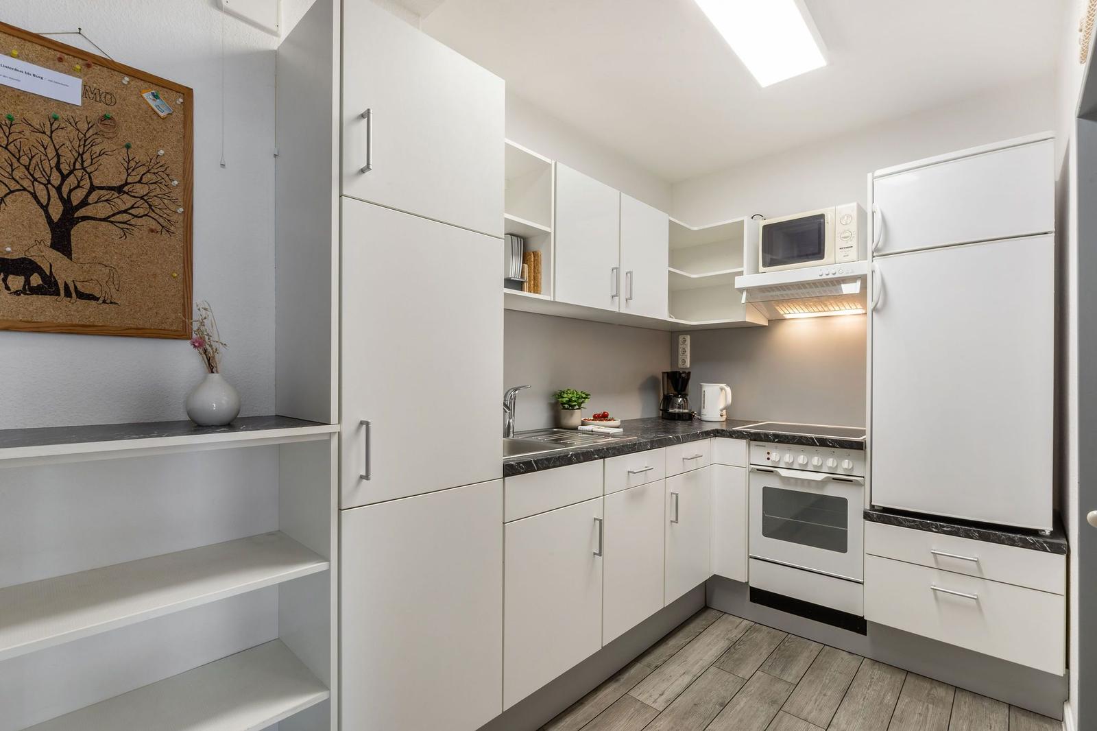 Küche mit weißen Schränken, Herd, Kühlschrank und Mikrowelle.