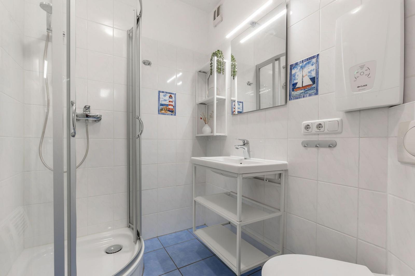 Badezimmer mit Dusche, Waschbecken und Toilette. Weiße Fliesen und blaue Bodenfliesen.