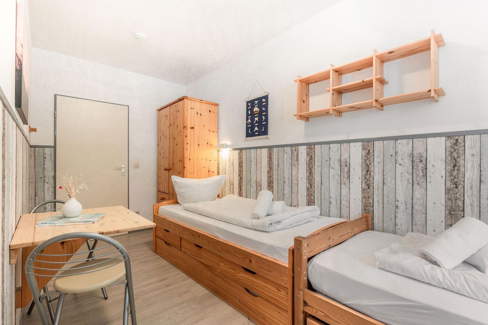Zimmer mit zwei Betten, Schreibtisch, Kleiderschrank und Wandregal.