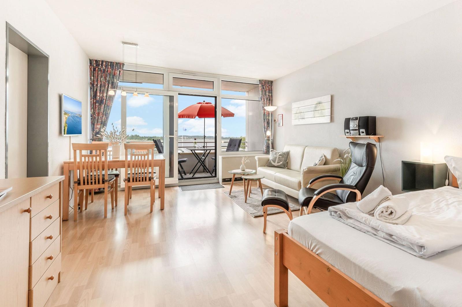 Wohnung mit Schlafzimmer, Wohn- und Essbereich sowie Balkon mit rotem Sonnenschirm.