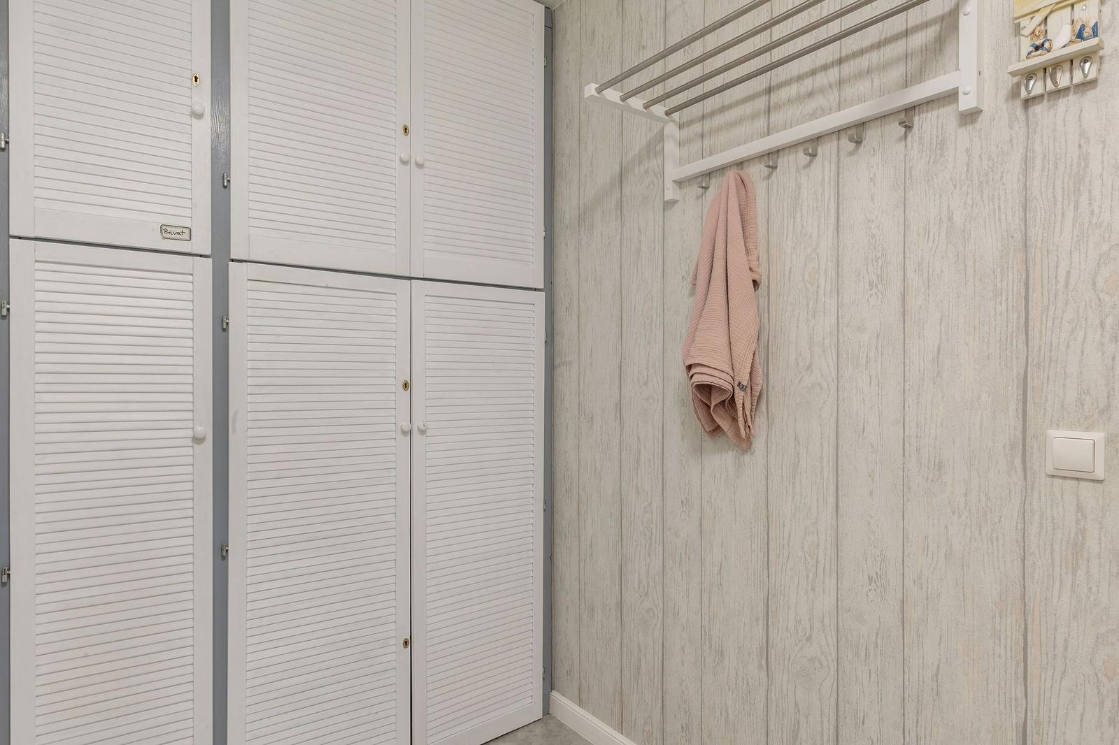 Wand mit Holzoptik, Kleiderständer und weißer Schrankwand mit Lüftungsschlitzen.