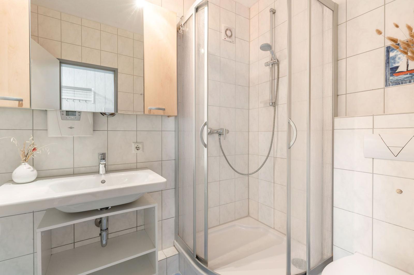 Badezimmer mit Dusche, Waschbecken und Spiegel.