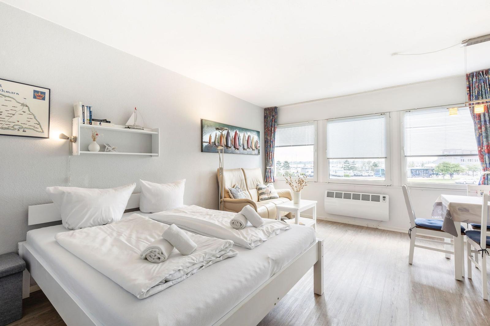 Schlafzimmer mit Bett, Sofa, Tisch und Fenstern mit Blick nach draußen.
