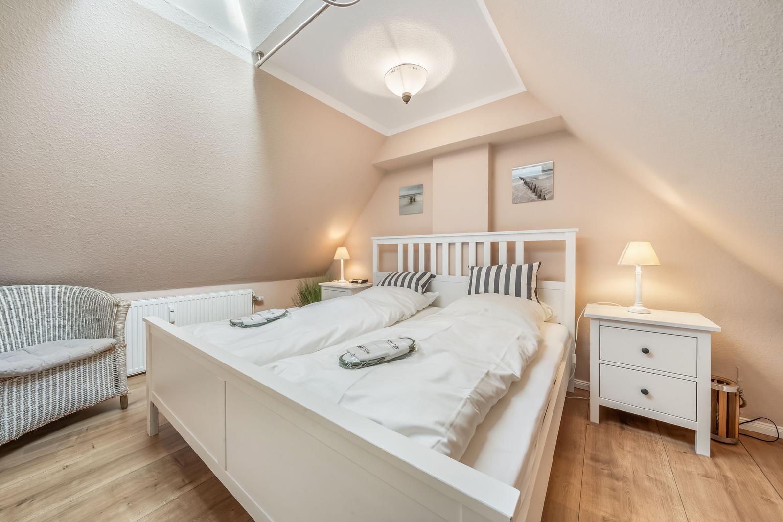 Bedroom with double bed, nightstands, and wicker chair under sloped ceiling.