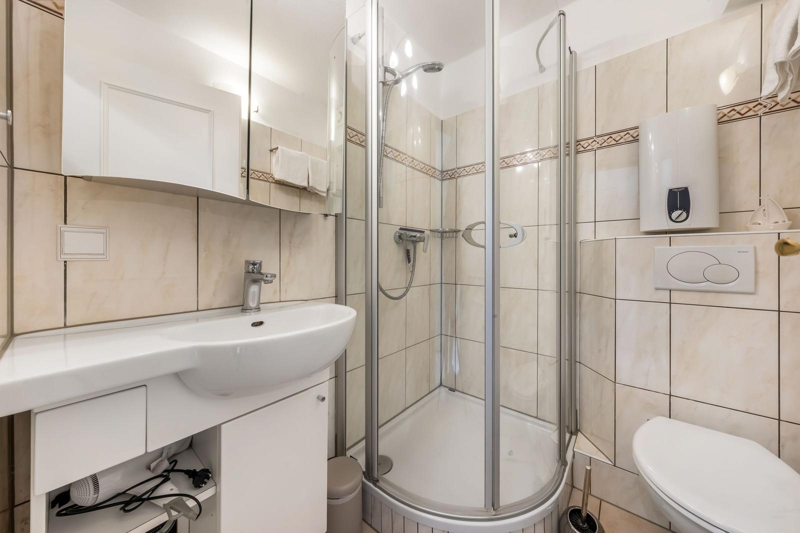 Bathroom with shower, sink, and toilet. Tiled wall and mirror cabinet.