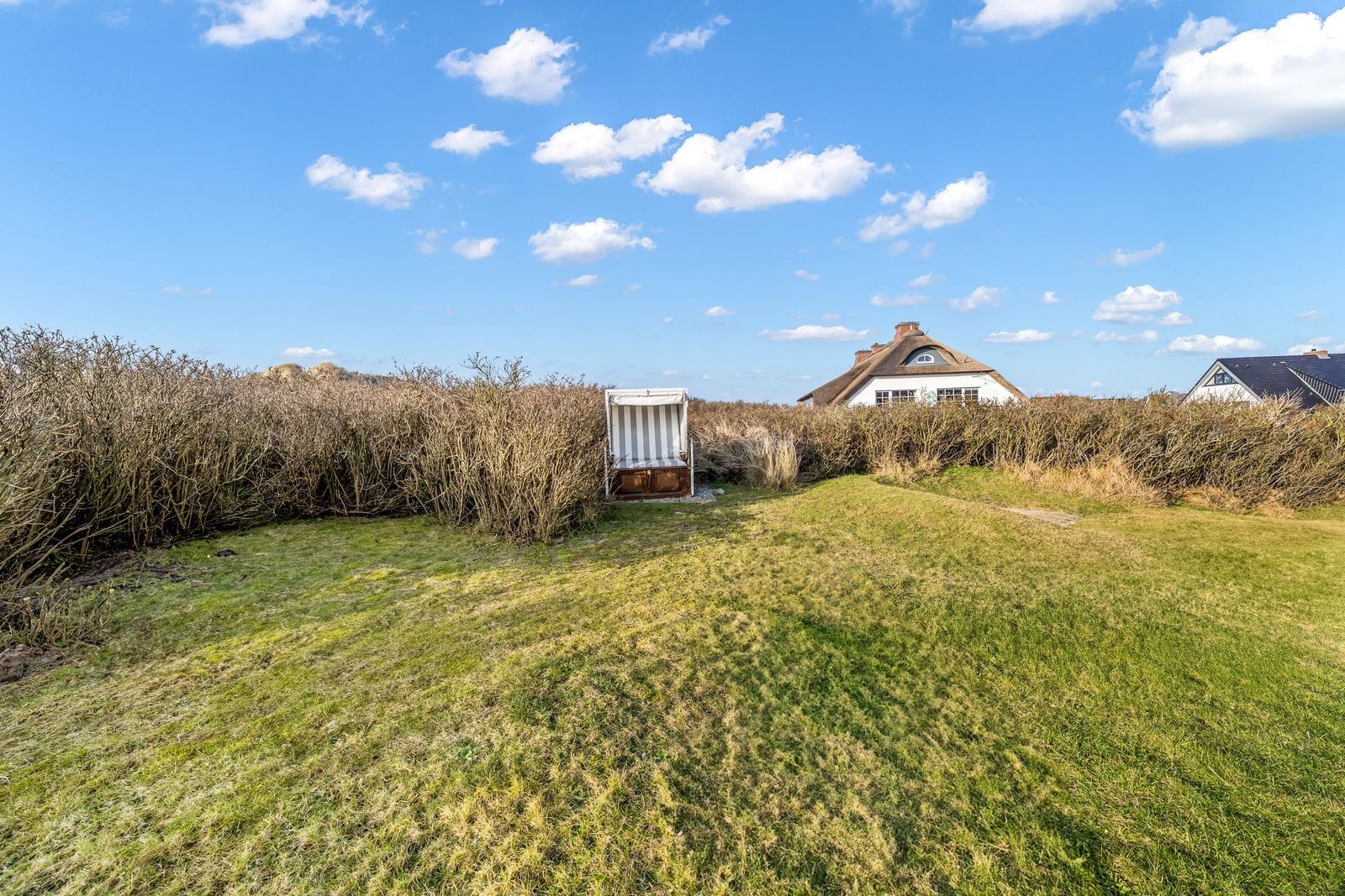 Green lawn area with beach chair and view of house with roof