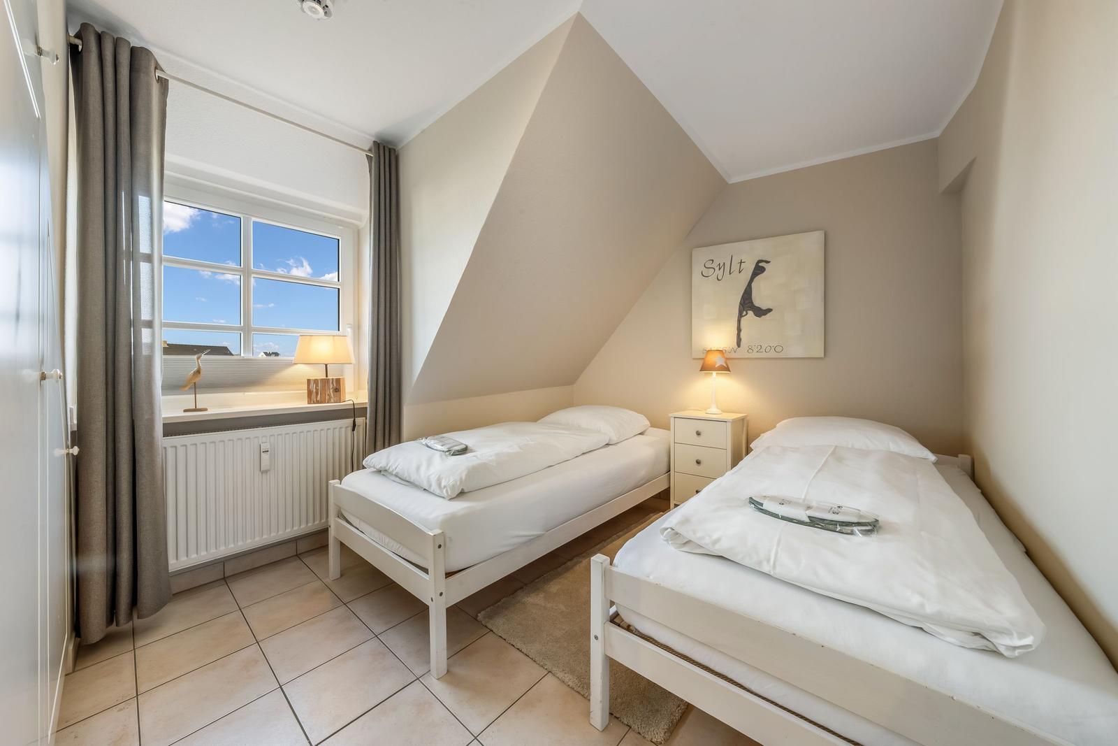 Two single beds in an attic room with window and nightstand.