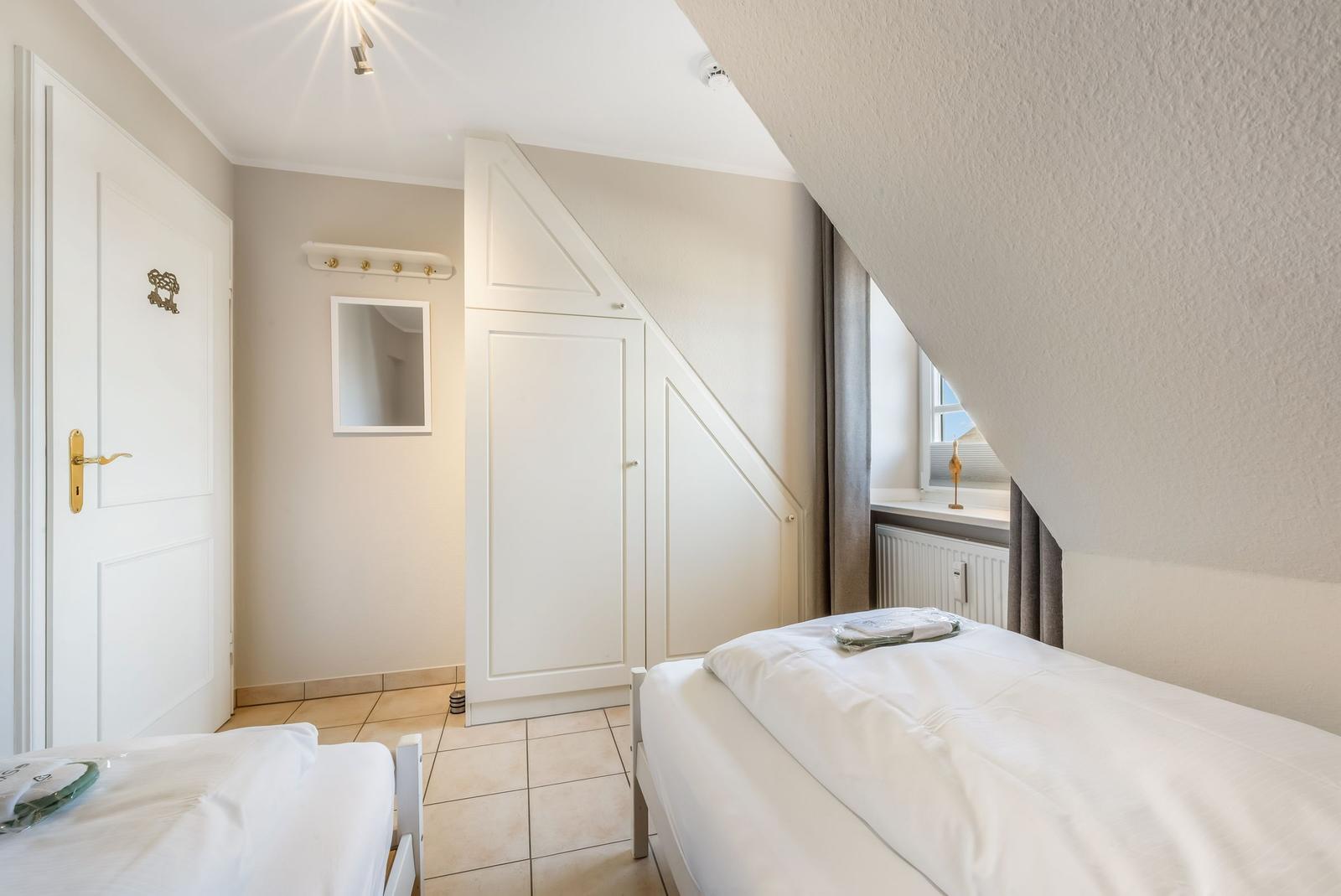 Bedroom with sloped ceiling, white bed, and wardrobe.