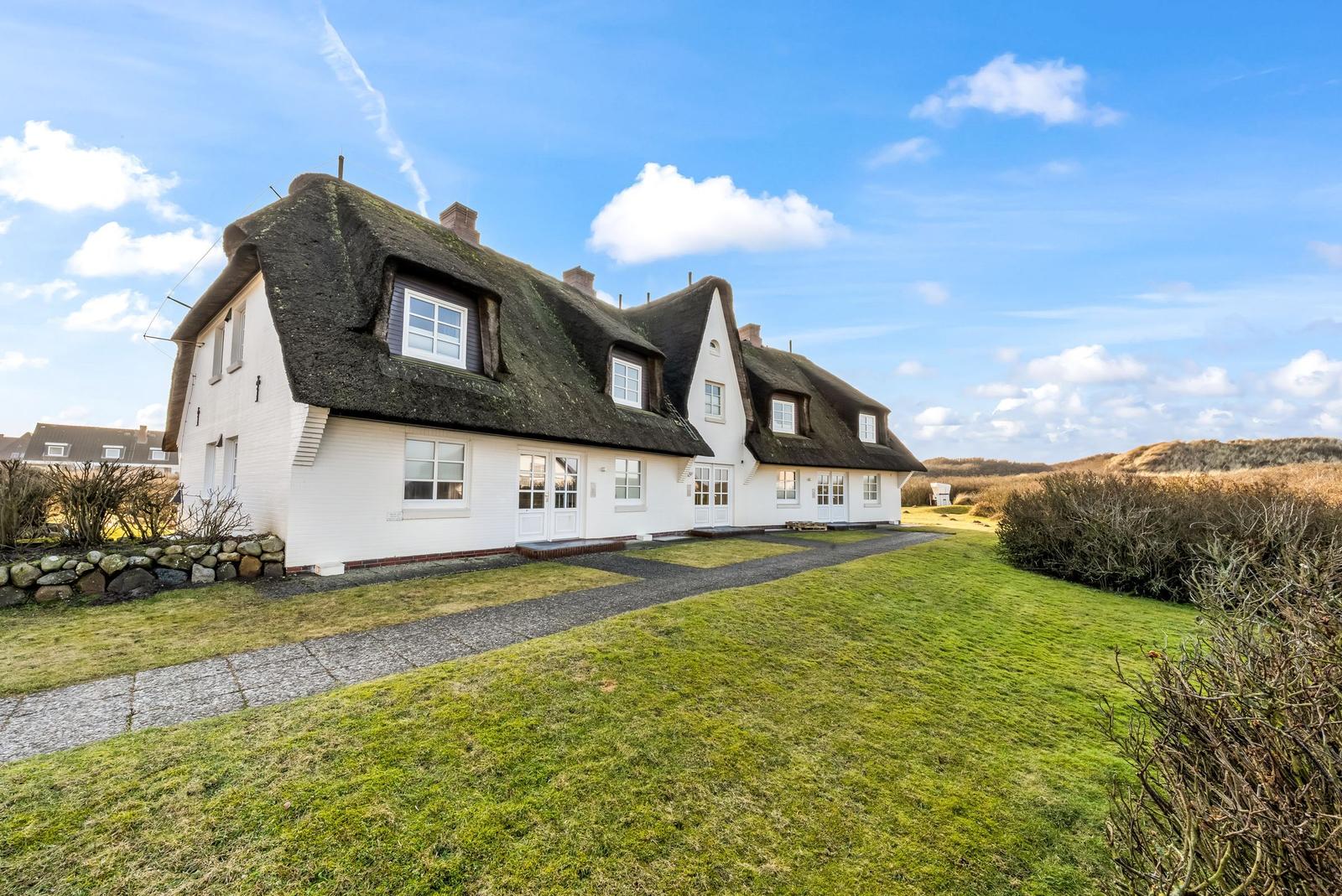 A white house with a thatched roof and multiple windows on a green lawn.