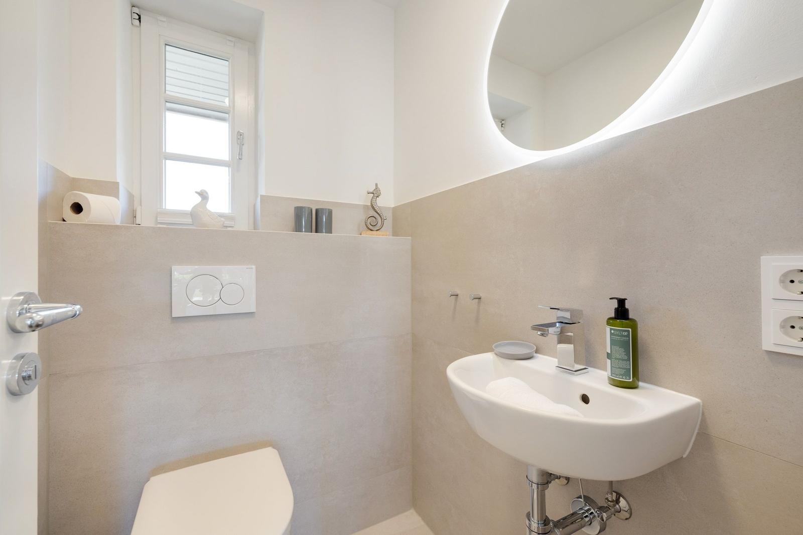 Badezimmer mit Waschbecken, Spiegel, Toilette und Fenster.