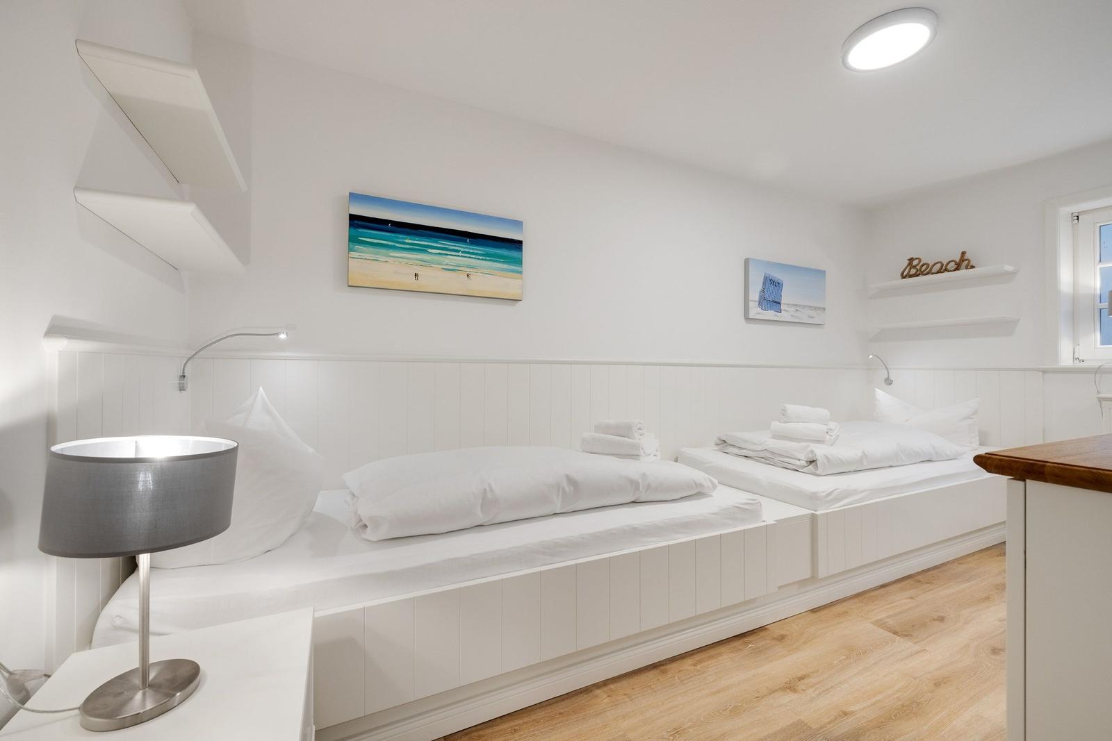 Zwei Matratzen auf Bodenlage mit weißen Laken und Kissen. Wandbild mit Strandmotiv.