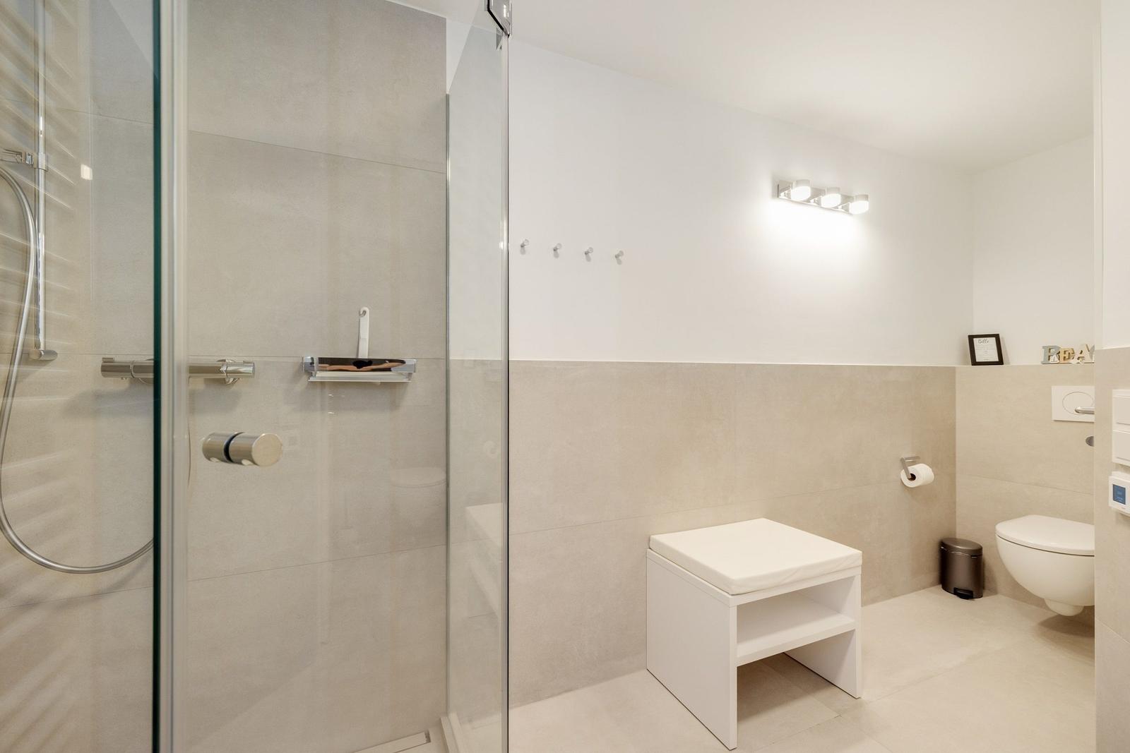 Dusche mit Glaswand, WC und Sitzbank in moderner Badezimmerausstattung.
