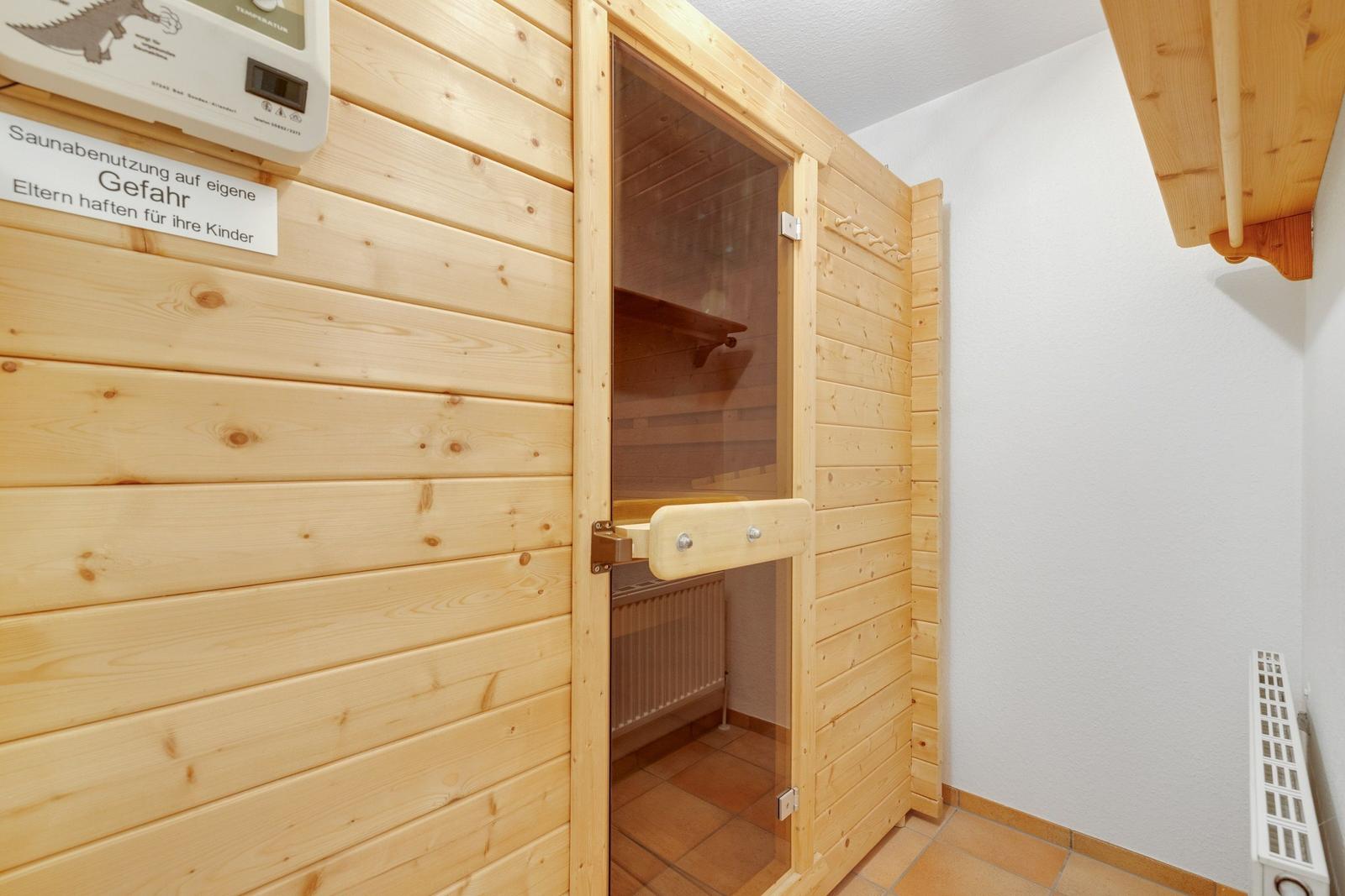 Holzsauna mit Tür und Sitzbänken. Anzeige für Saunabenutzung auf eigene Gefahr.