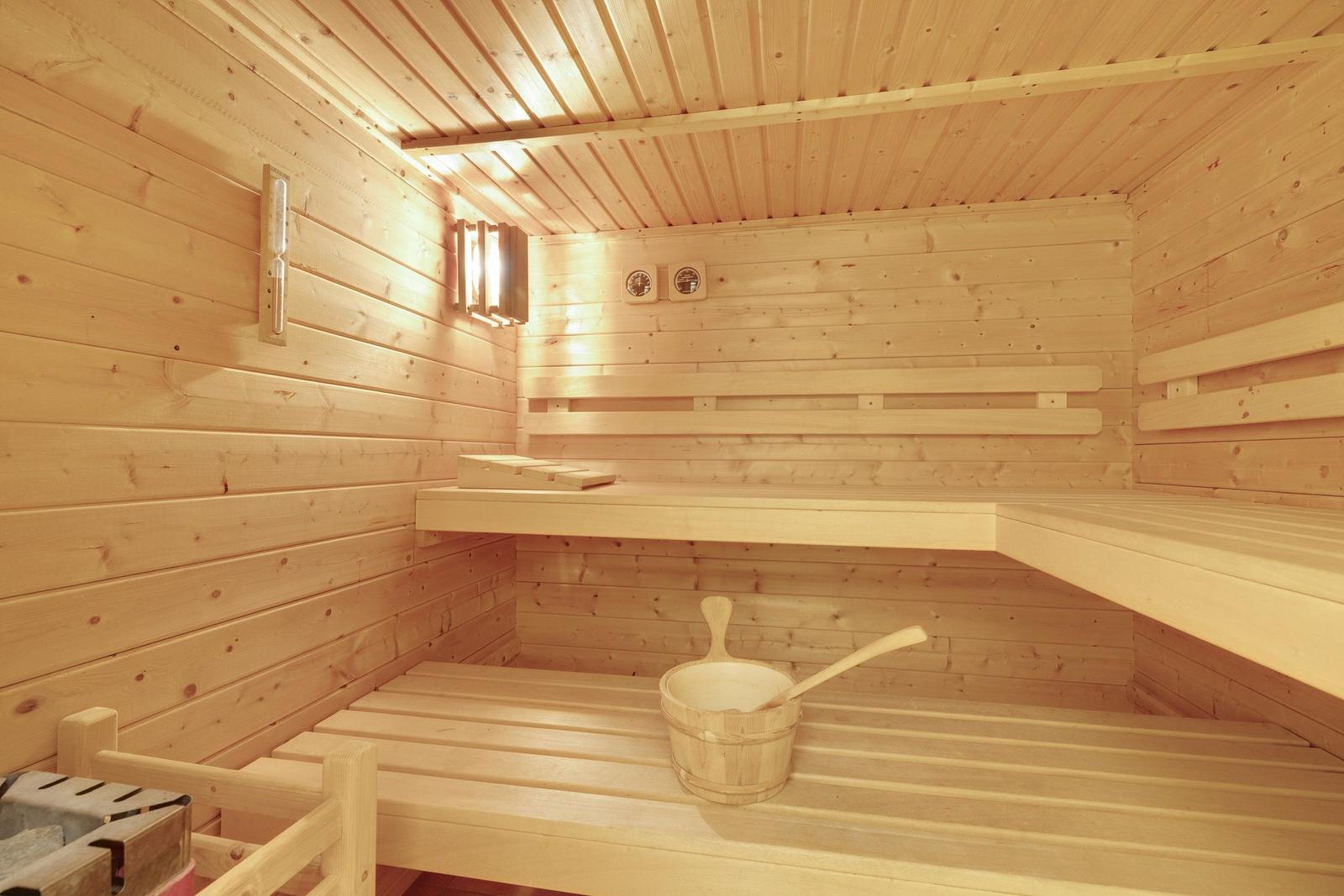 Sauna mit Holzbanken, Thermometer und Eimer mit Löffel.