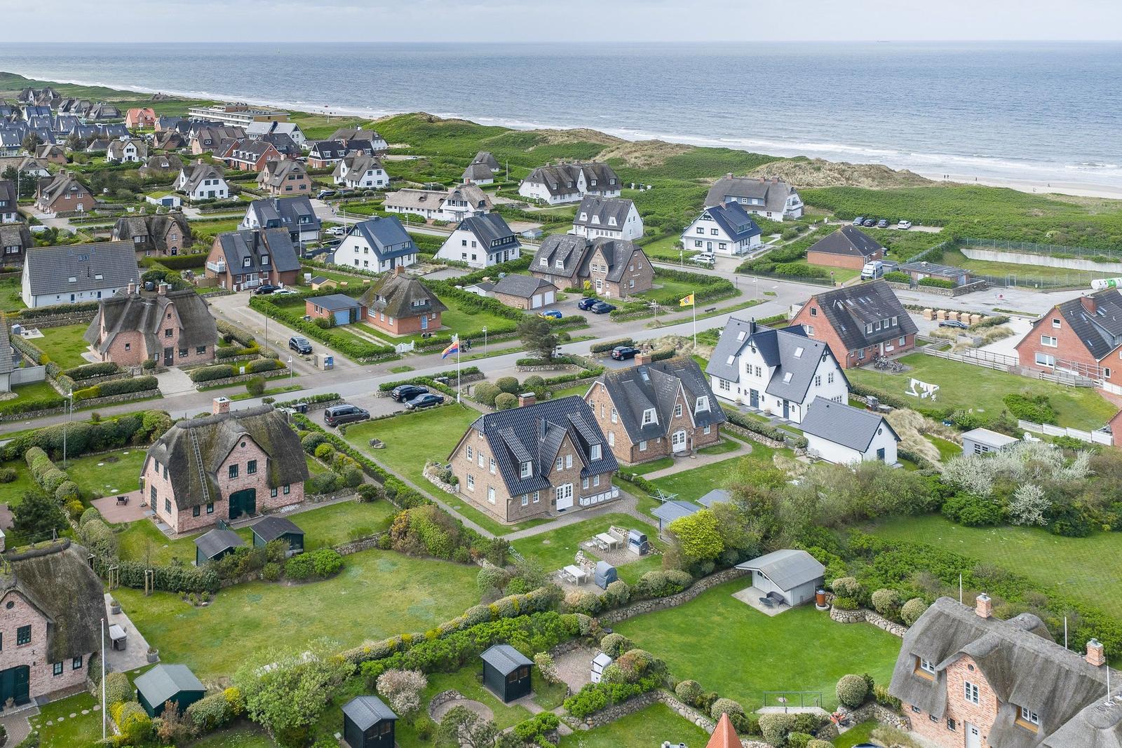 Aerial view of coastal village with traditional houses and green lawns near the sea.