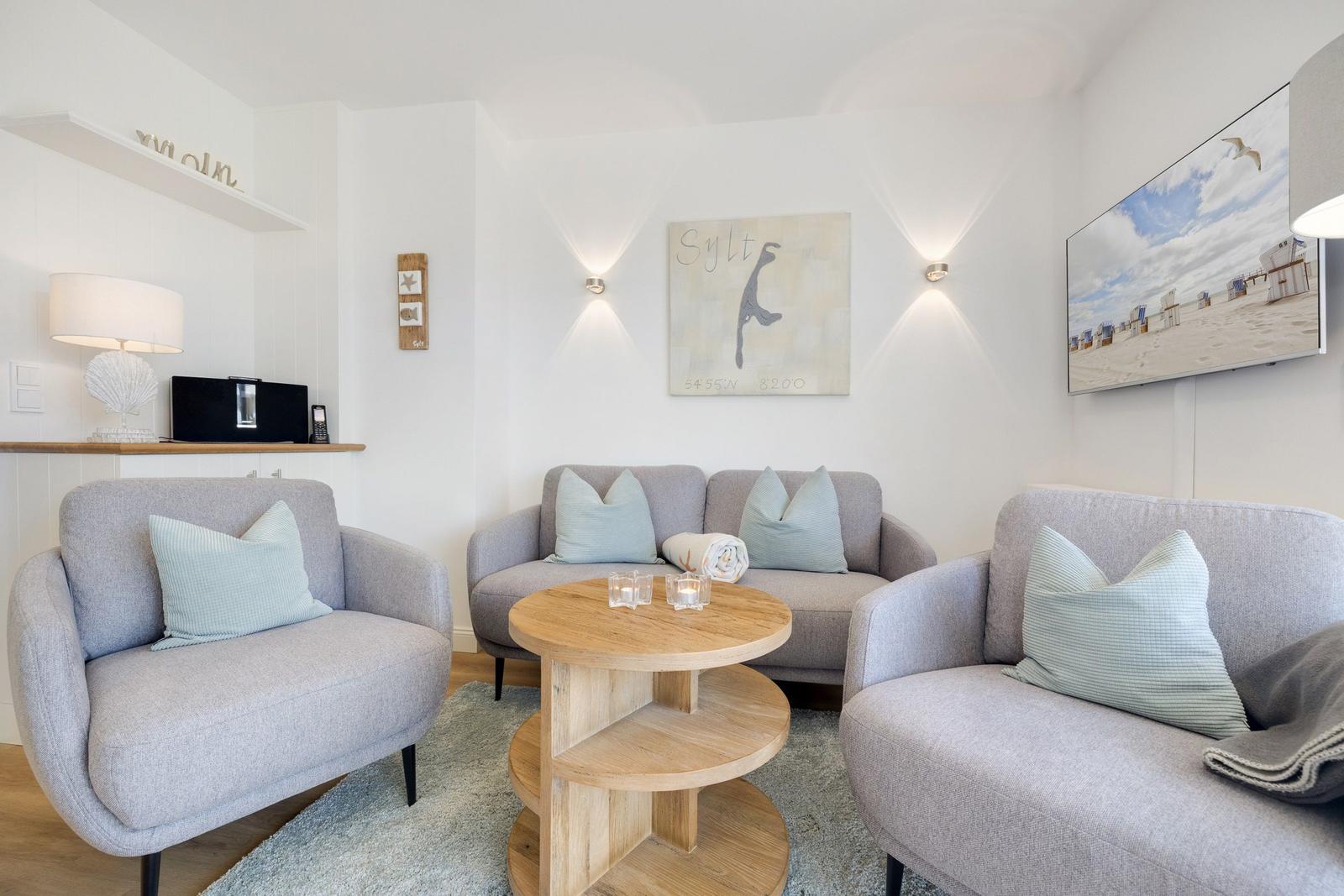 Wohnzimmer mit grauen Sesseln, Holztisch und Strandbild an der Wand.