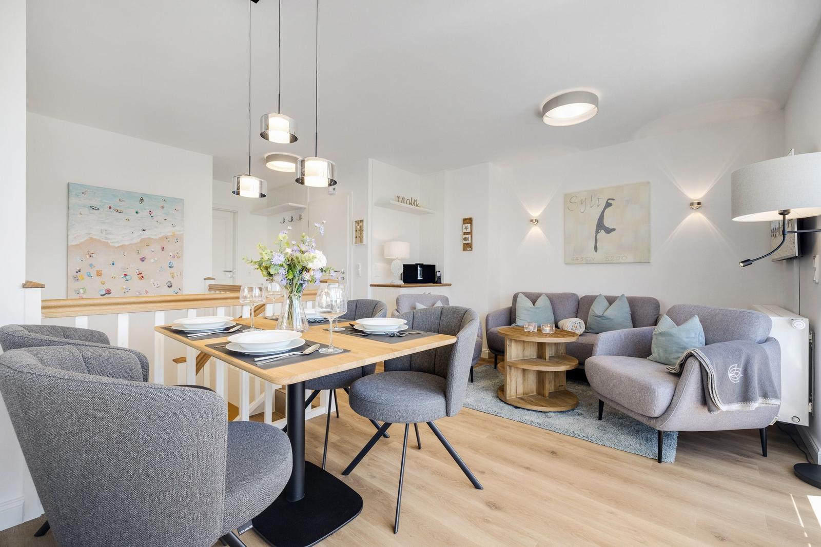 Essbereich mit Tisch und Stühlen. Wohnbereich mit Sofa und Sessel. Wandbilder und Beleuchtung.