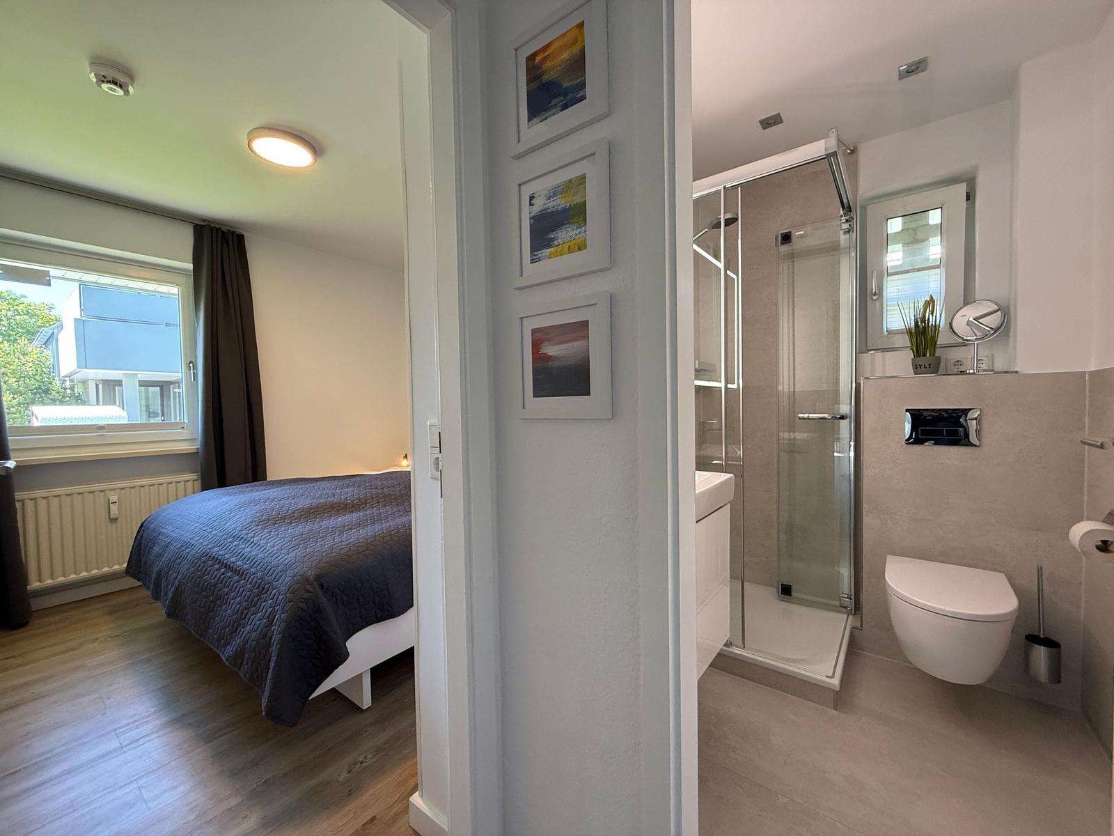 Schlafzimmer mit Bett und Fenster. Nebenraum mit Dusche, Toilette und Waschbecken.