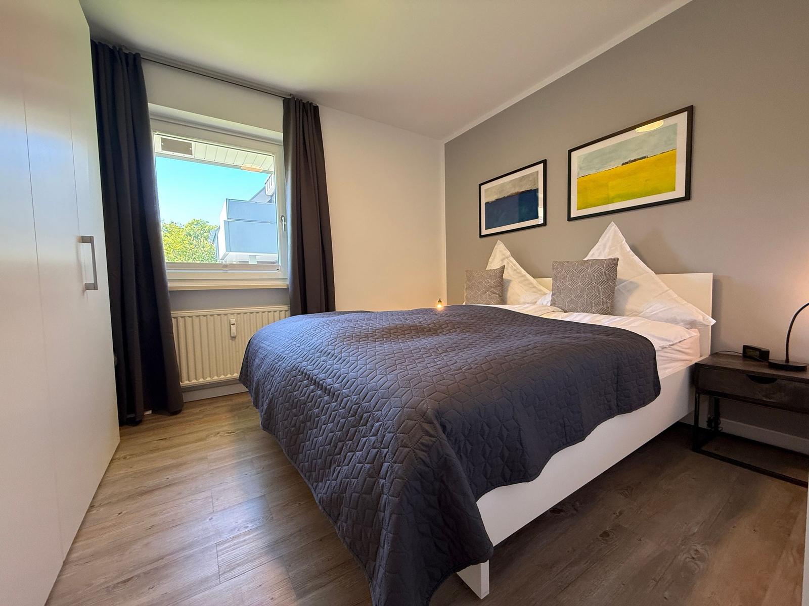 Schlafzimmer mit Bett, Fenster und Wandbildern.