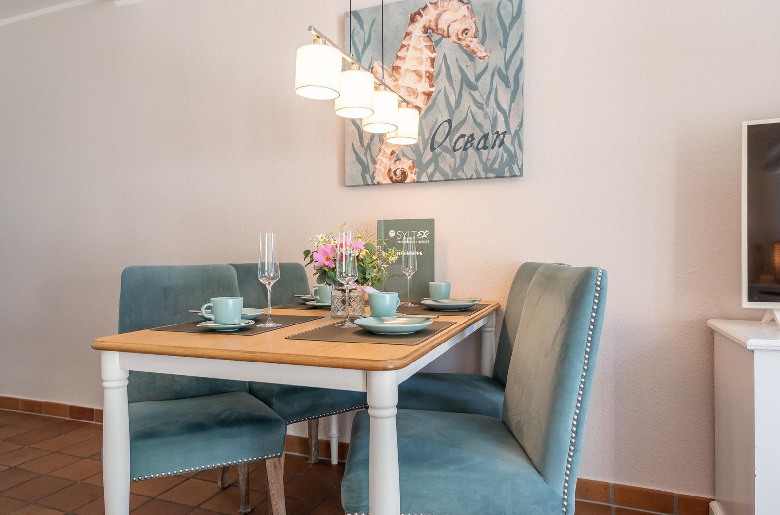 Esszimmer mit Tisch, Stühlen und Wandbild mit Seepferdchen.