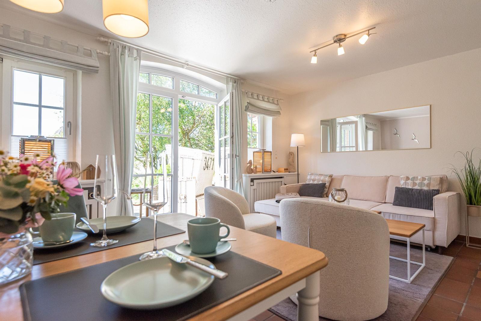 Wohn- und Essbereich mit Sofa, Stühlen und Tisch. Fenster und Tür führen auf Balkon.