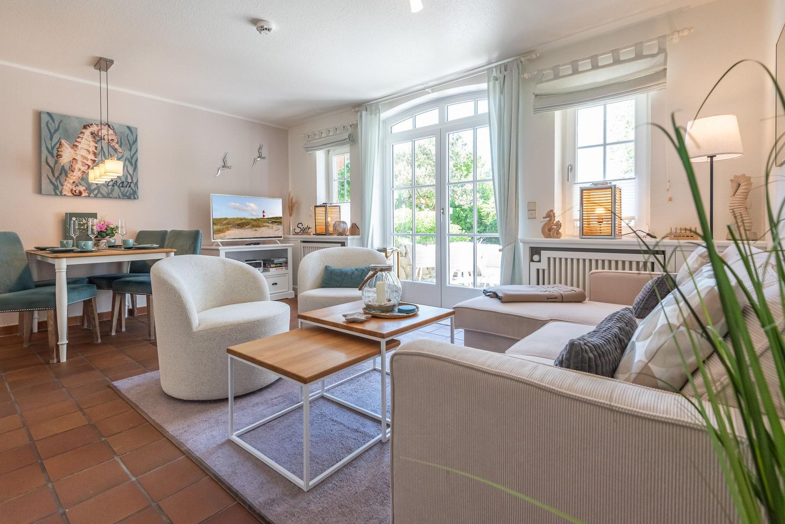 Wohn- und Essbereich mit Sofa, Stühlen und TV. Große Fenster und Terrasse.