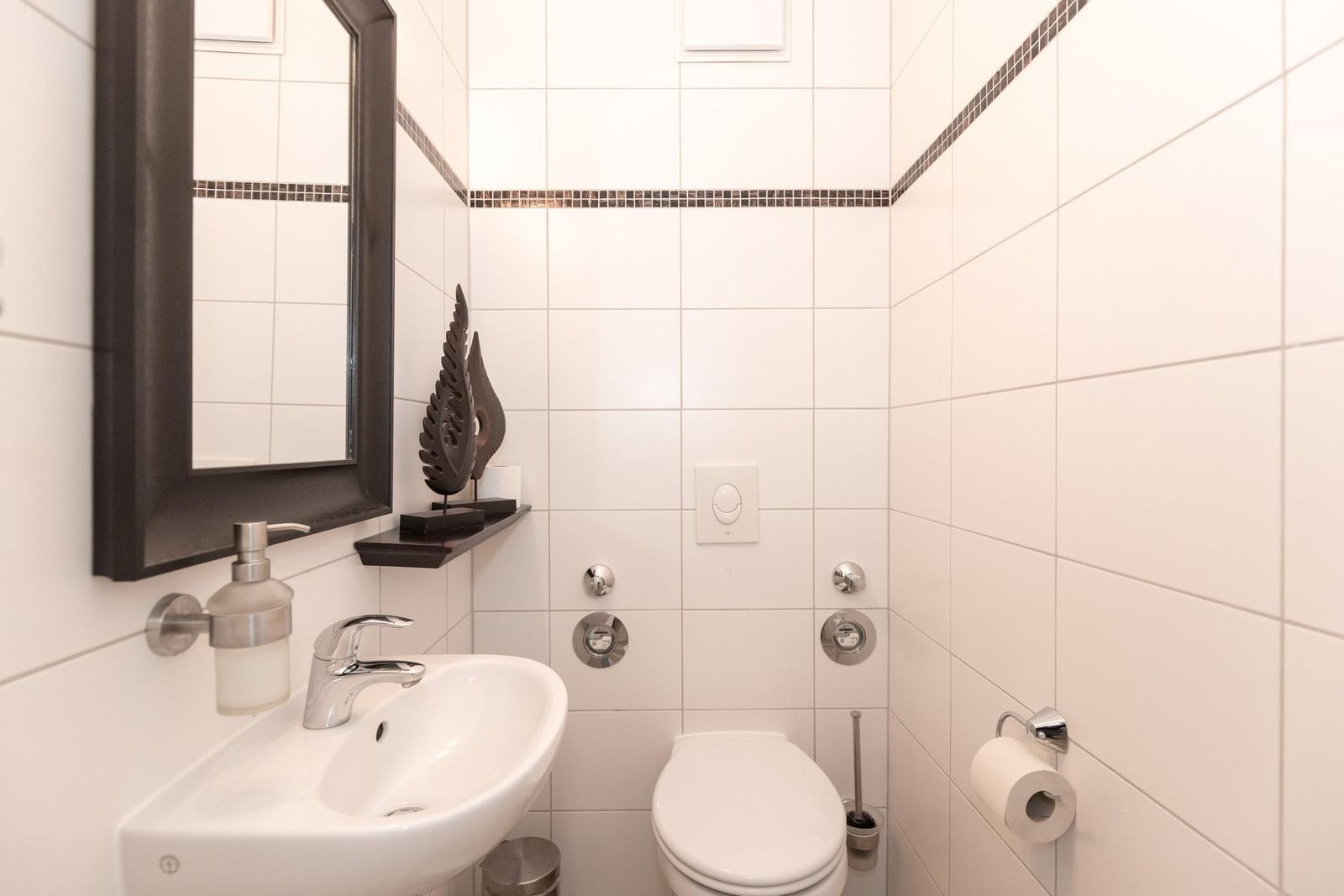 Badezimmer mit Waschbecken, Spiegel, Toilette und Toilettenpapierhalter.