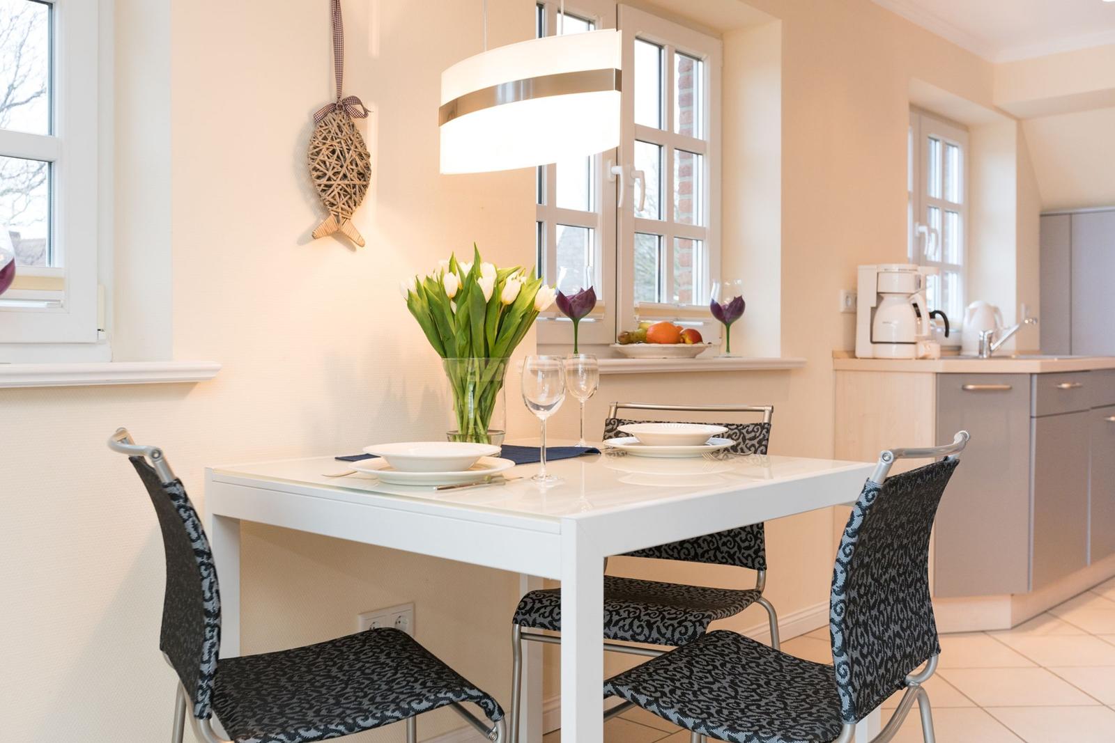Essbereich mit weißem Tisch, vier Stühlen und Blumen auf dem Tisch.