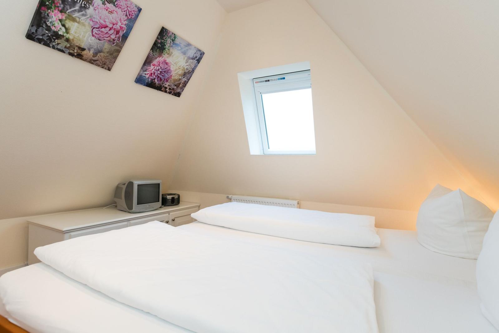 Schlafzimmer mit Dachschrägen, Fenster und Bett mit weißer Bettwäsche.
