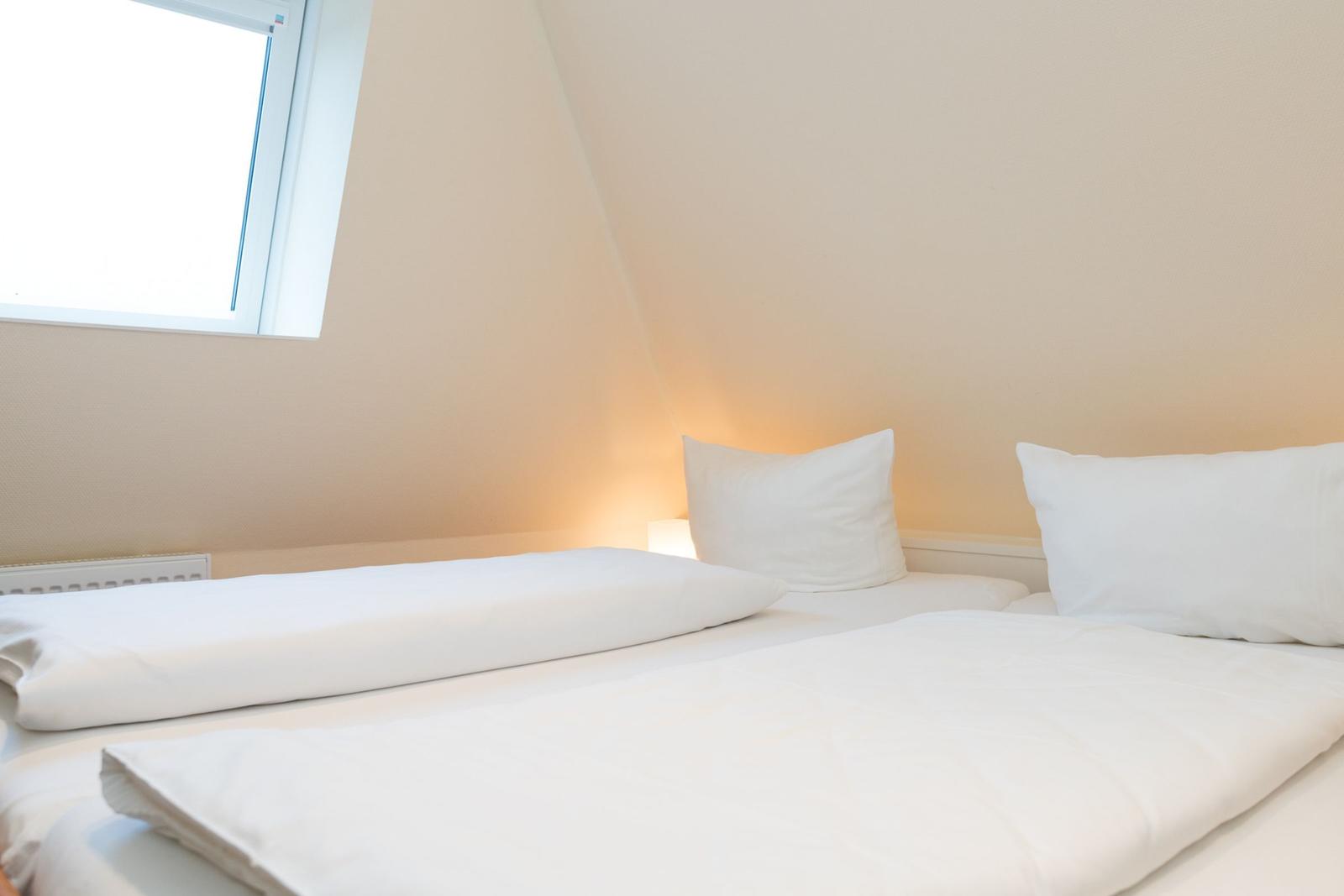 Schlafzimmer mit Doppelbett, weißer Bettwäsche und Fenster