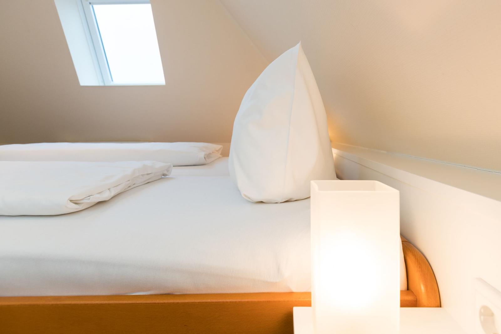 Schlafzimmer mit weißem Bett, Fenster und Nachttischlampe.