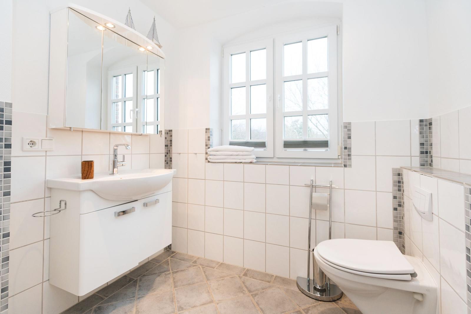 Badezimmer mit Waschbecken, Spiegel, Toilette und Fenster.