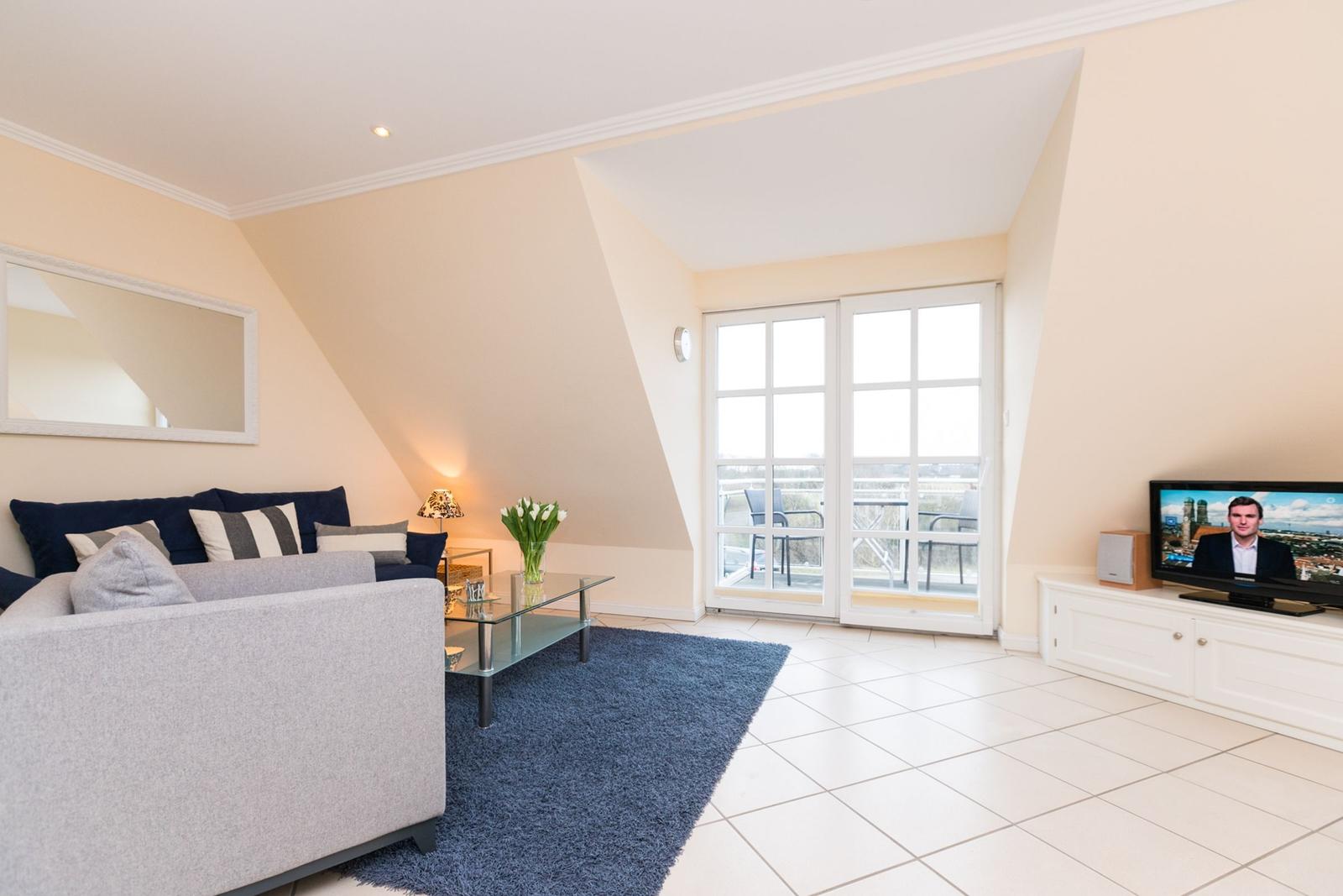 Wohnzimmer mit Sofa, Glas-Tisch, Fernseher und Balkontür.
