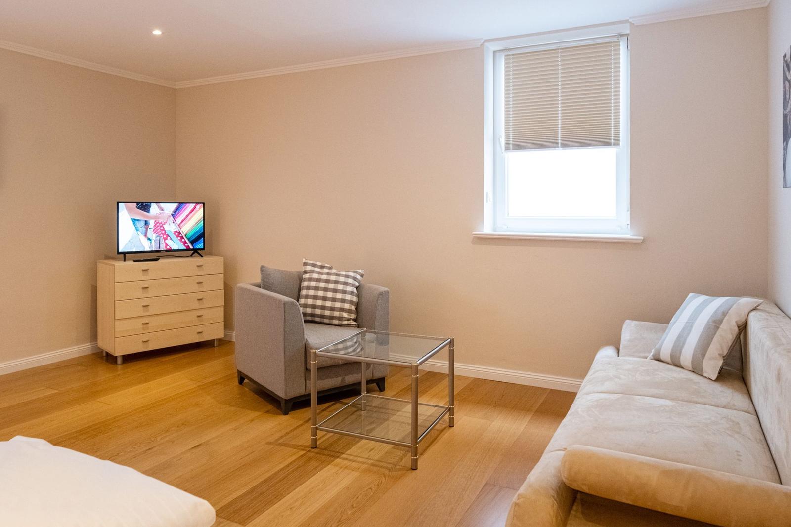 Wohnzimmer mit Sofa, Sessel, Glas-Tisch und Fernseher auf Schrank