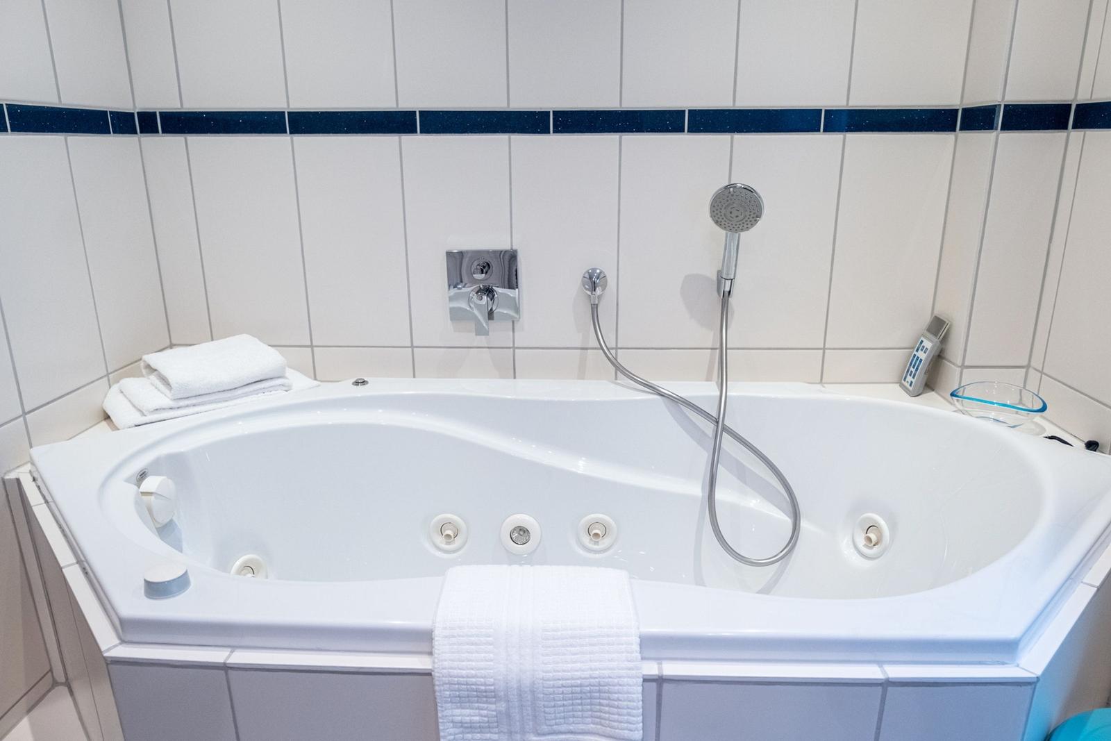 Duschbadewanne mit Handbrause und weißen Handtüchern in einem hellen Badezimmer.