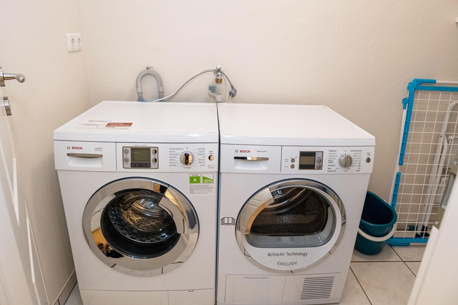 Waschmaschine und Trockner in einem Raum mit Fliesenboden und Wäscheschrank.
