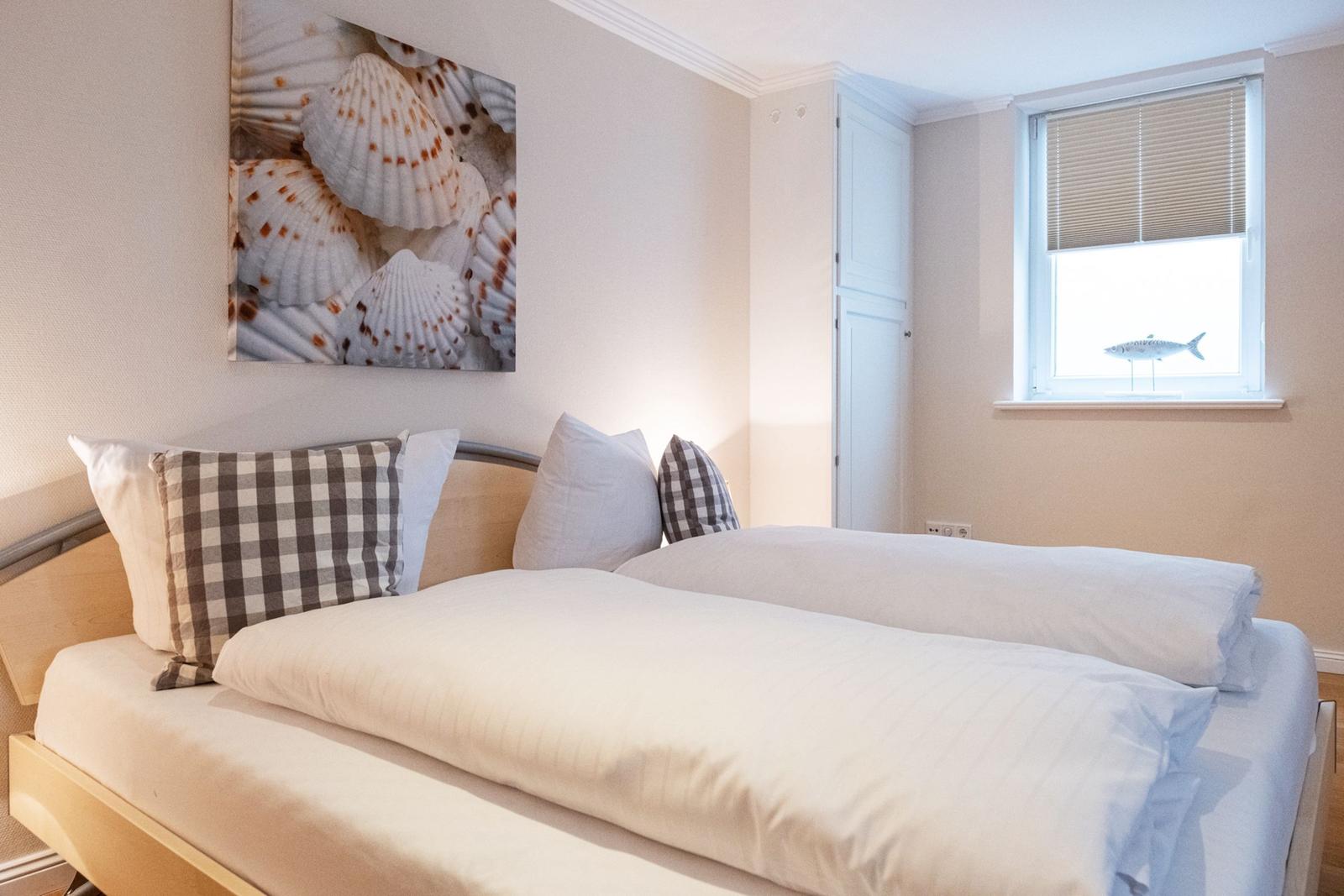 Schlafzimmer mit Bett, Wandbild von Muscheln und Fenster mit Fischdekoration.