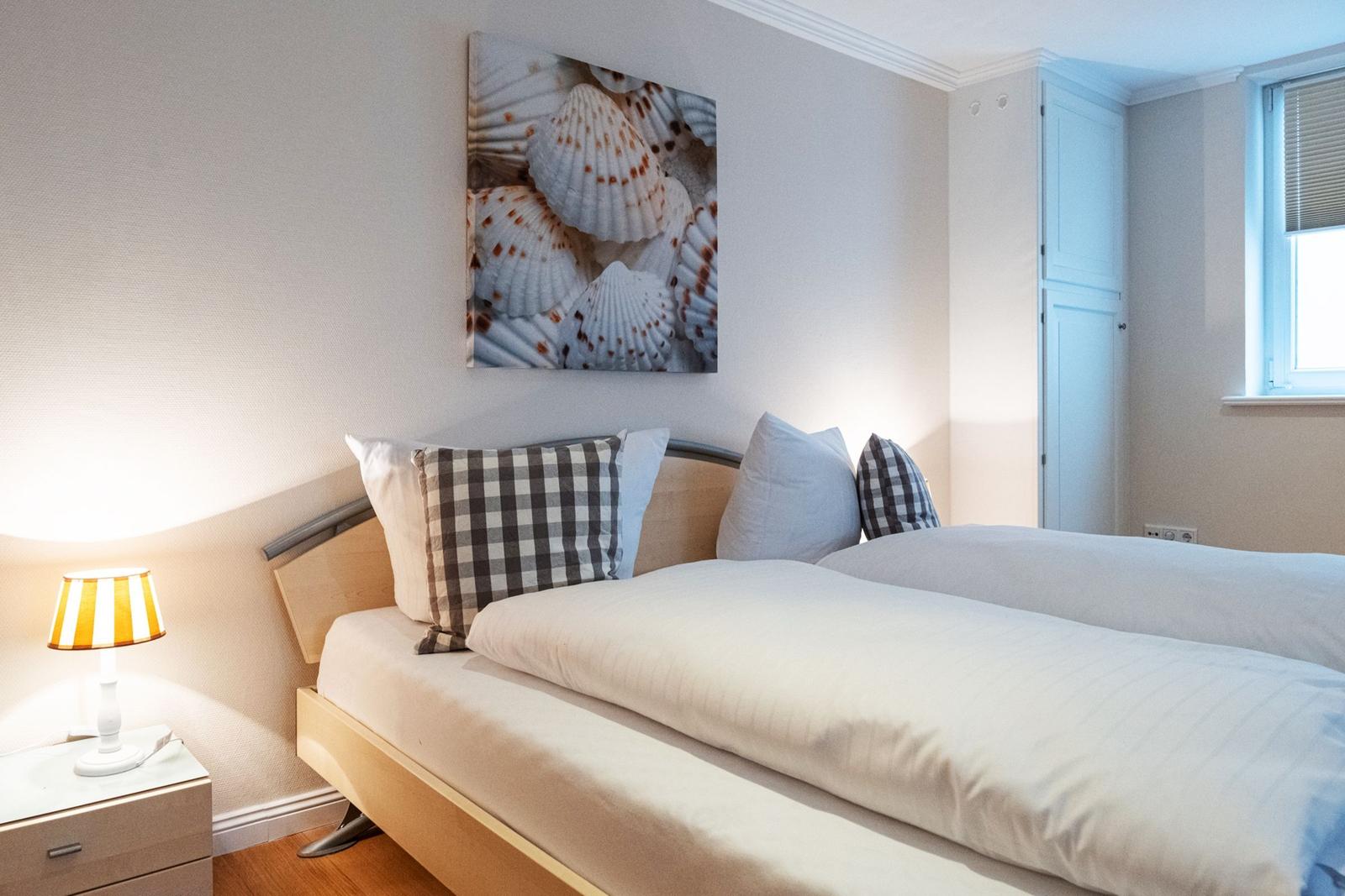 Schlafzimmer mit Doppelbett, Nachttisch und Wandbild mit Muscheln.
