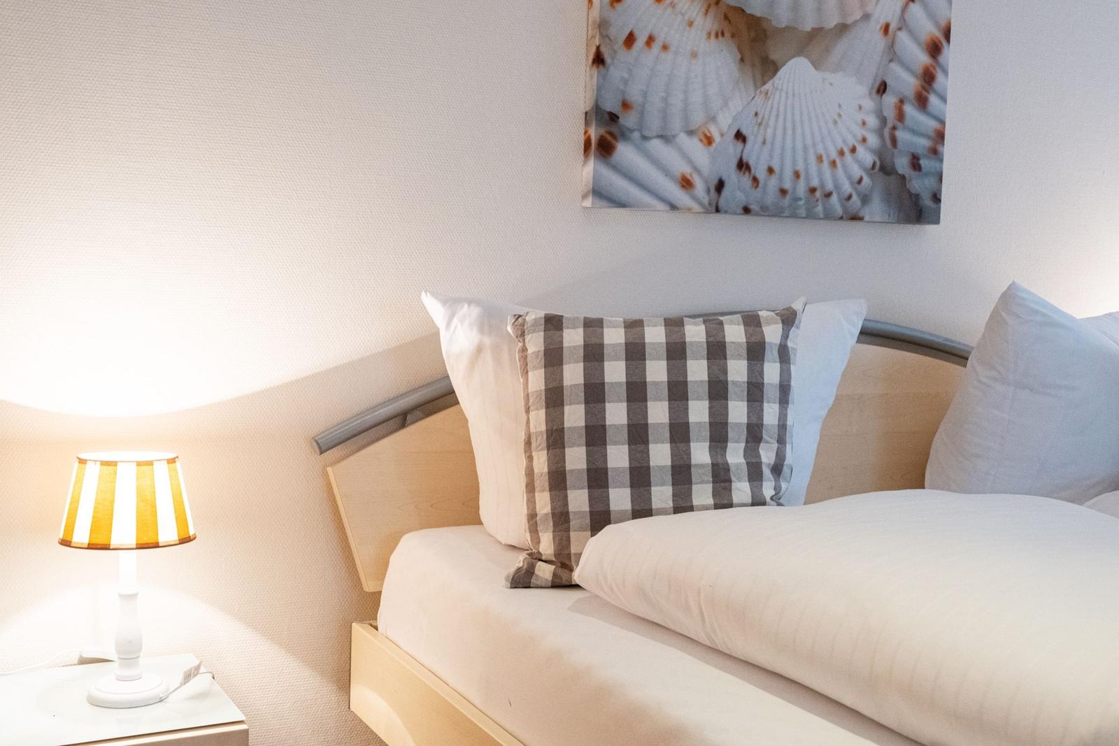 Schlafzimmer mit Bett, Kissen und Wandbild mit Muscheln.