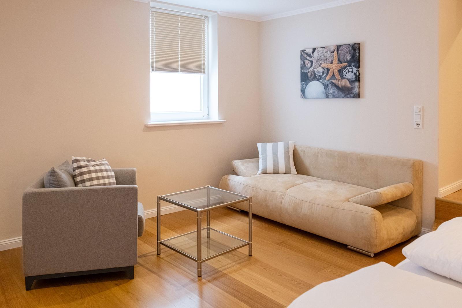 Wohnzimmer mit Sofa, Sessel und Glas-Tisch. Wandbild mit Muscheln und Seestern.