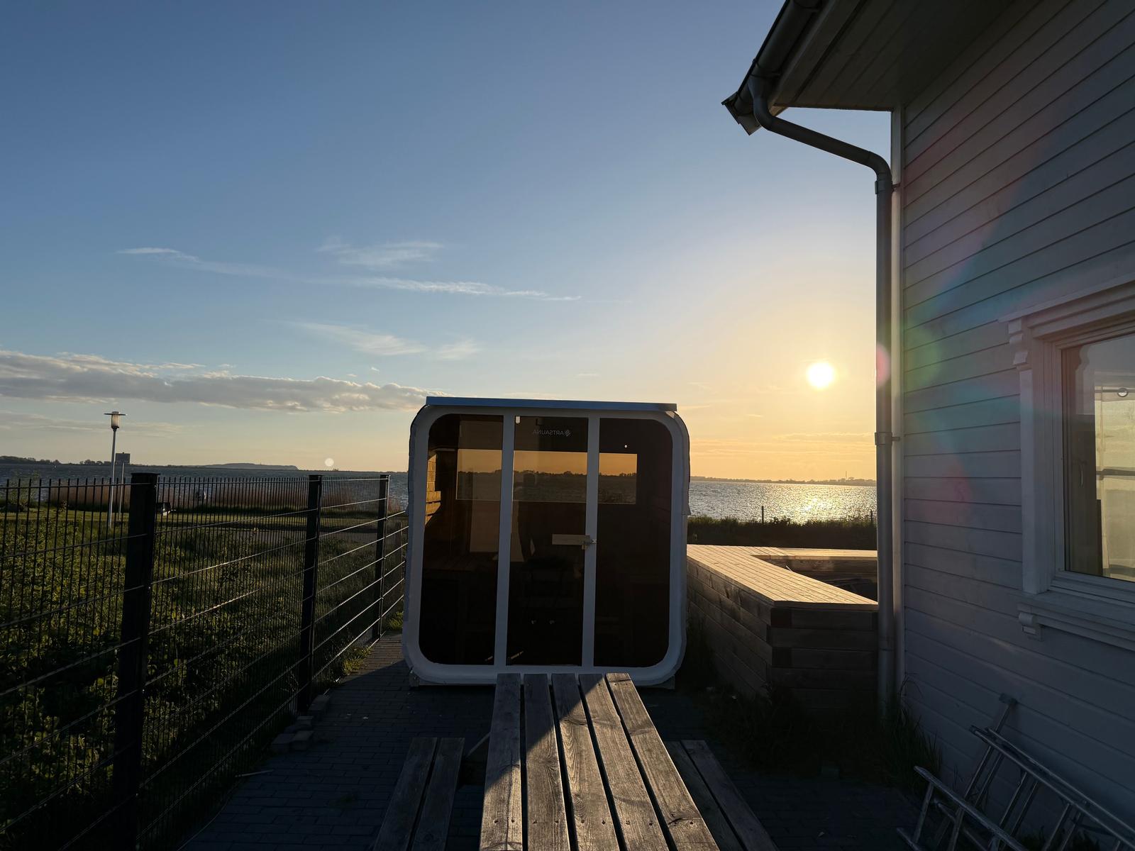 Außenliegende Sauna mit Blick auf Wasser und Sonnenuntergang neben Haus.