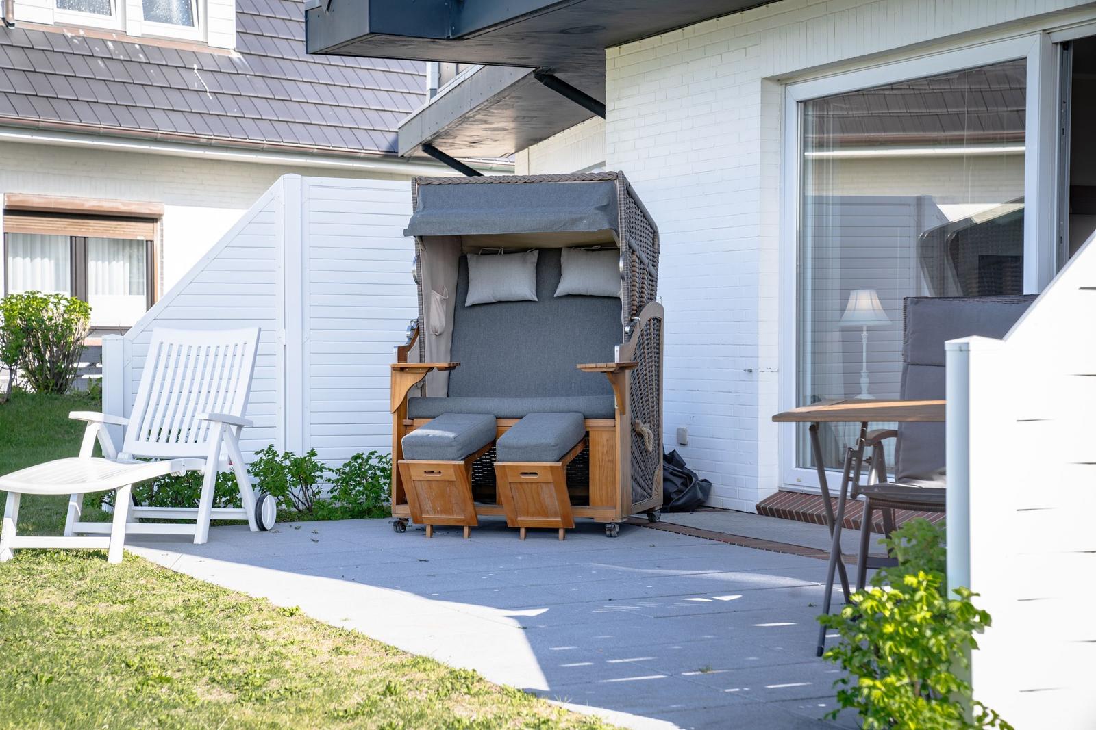 Terrace with lounge chair, sun cover, and table. Background: white house with window.