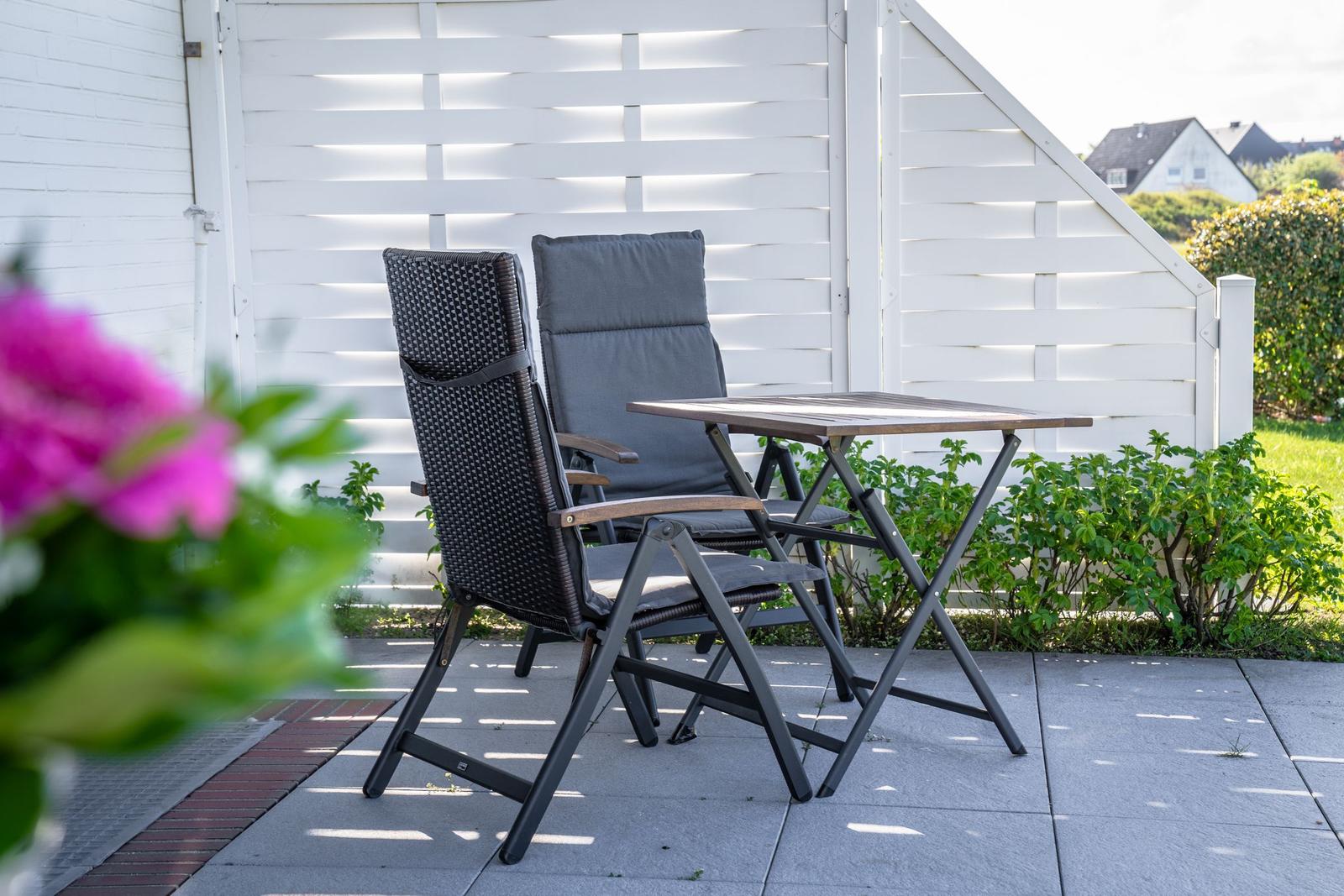 Outdoor area with table and two chairs in front of white wood paneling.