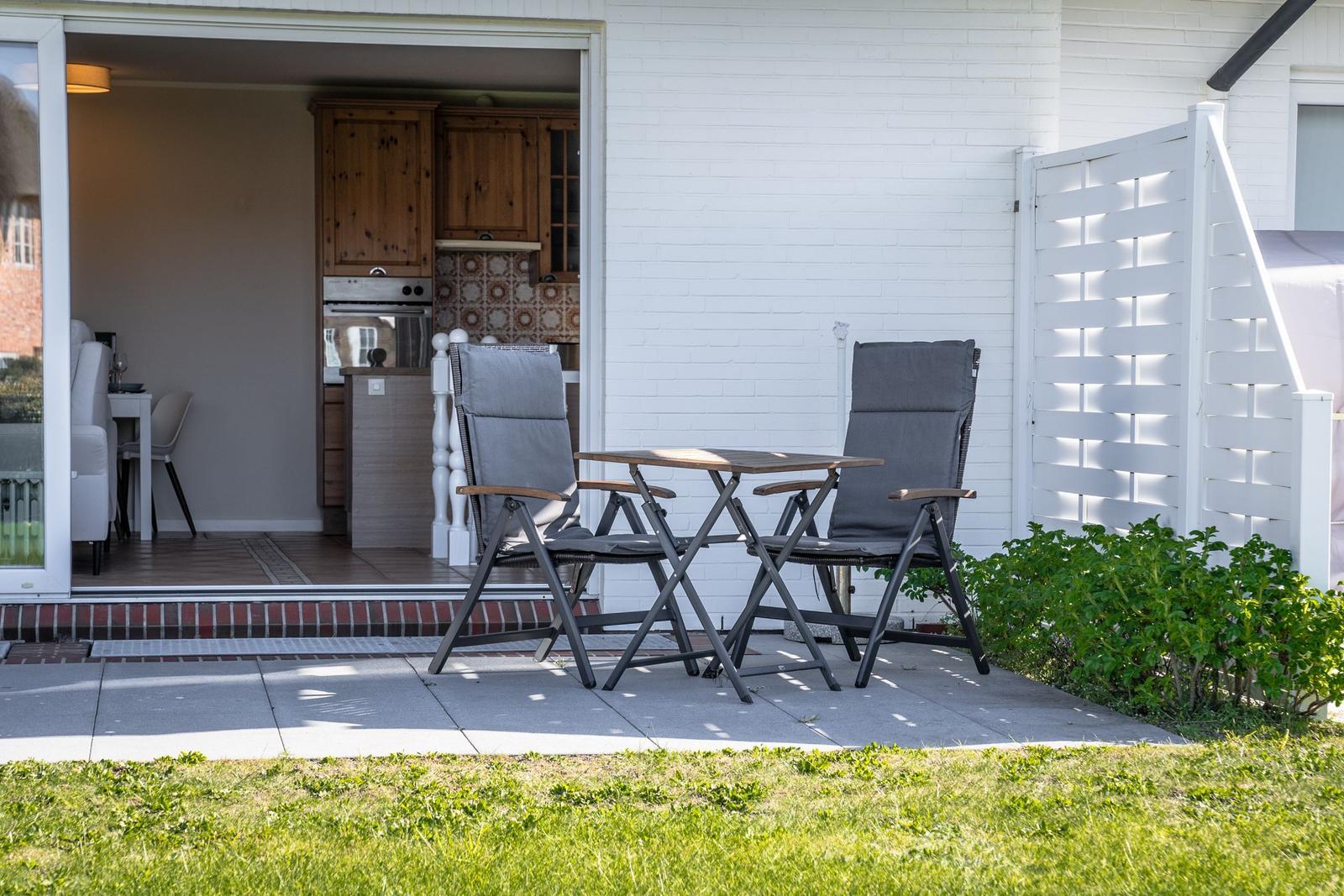 Terrace with table and two chairs. Kitchen visible in the background.
