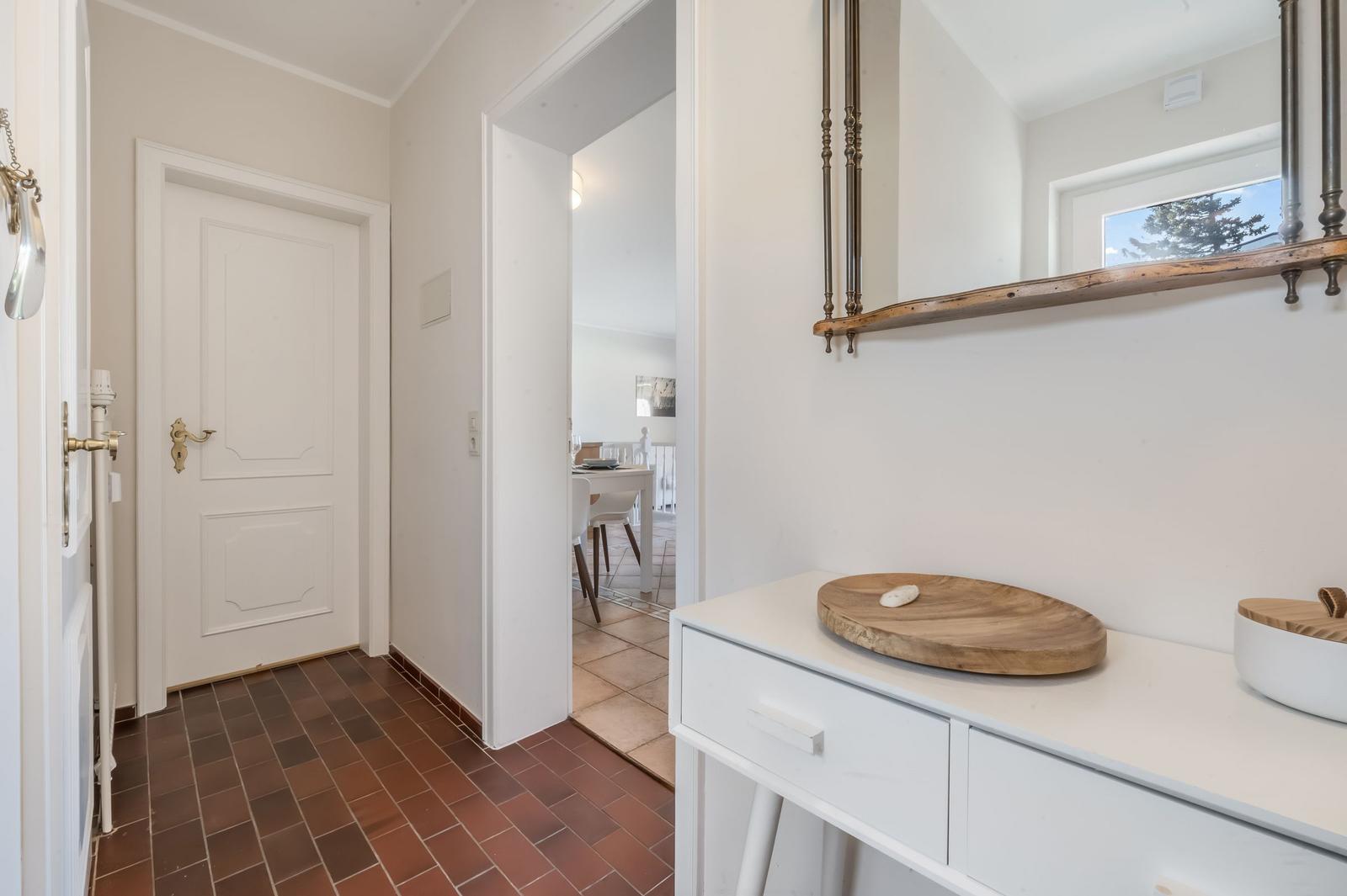 Hallway with white walls, brown floor, and mirror above cabinet
