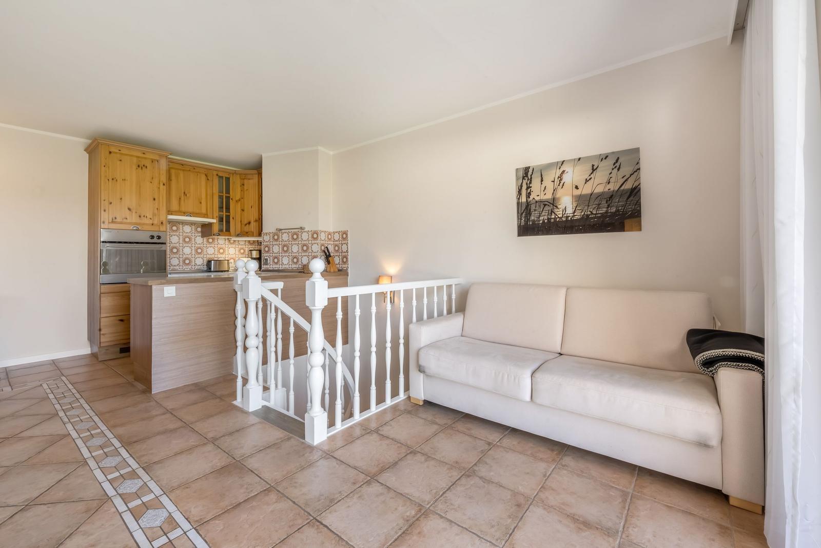 Living area with sofa, kitchen area, and staircase with white balustrade.