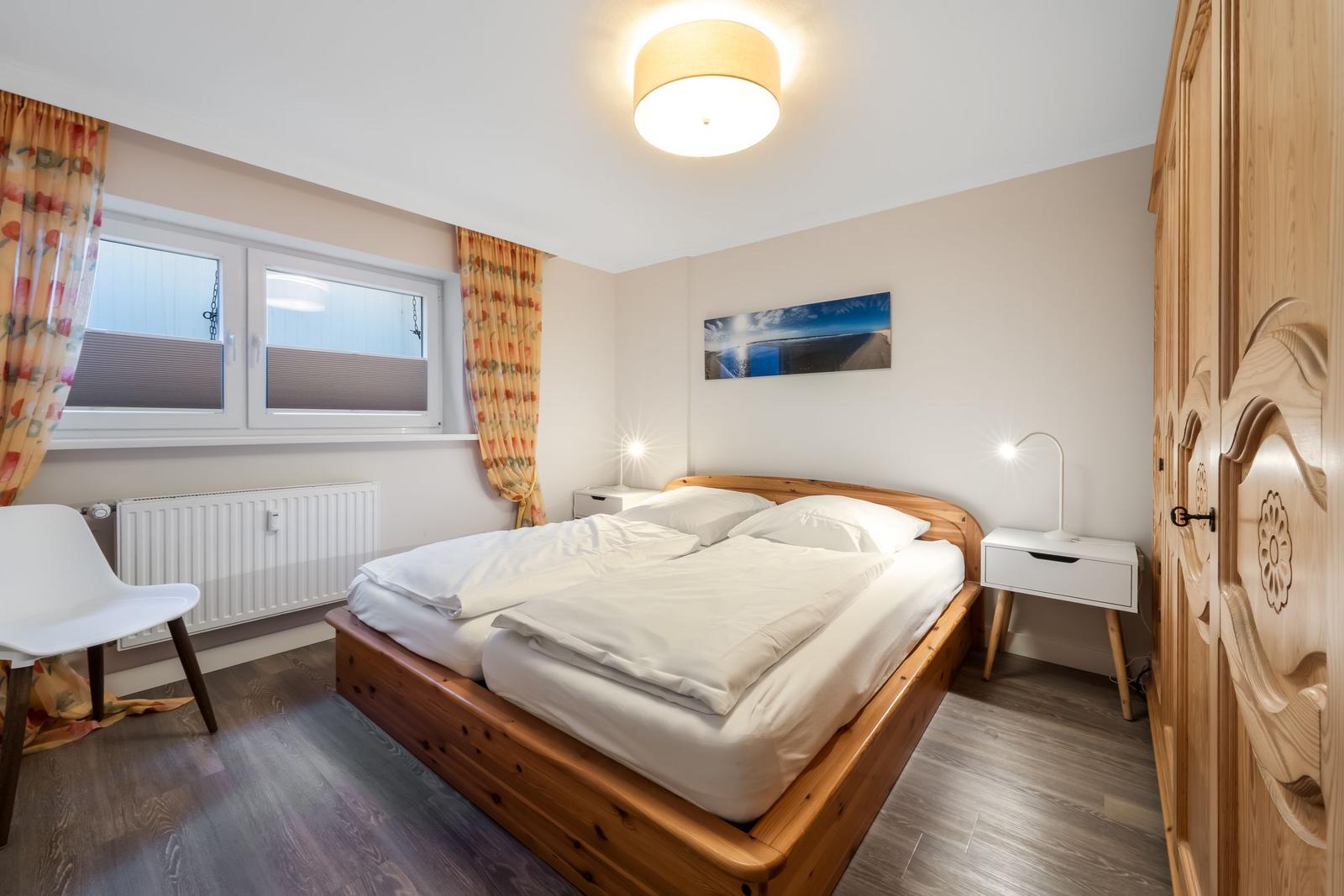 Bedroom with wooden bed, white nightstands, and wooden wardrobe. Window with floral curtains.