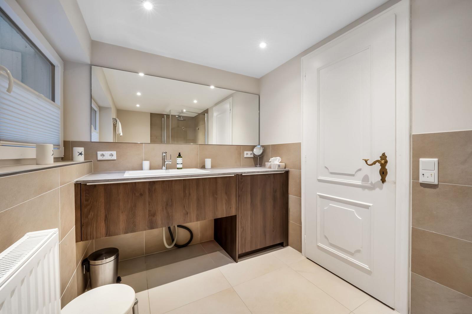 Bathroom with sink, mirror, toilet, and window.